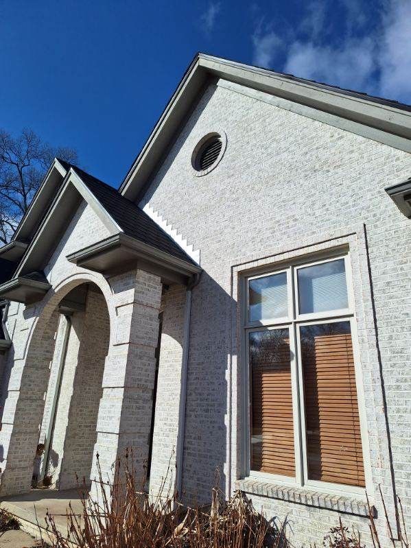 White brick house with a round window, arched entryway, and dark roof against a blue sky.