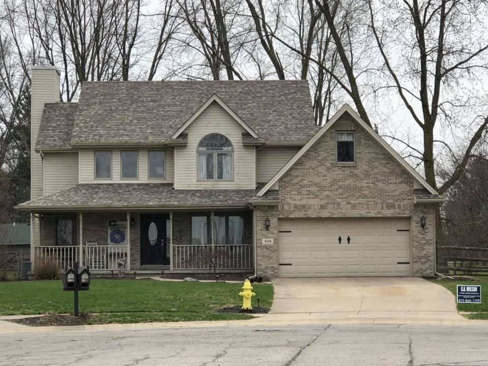 Two-story house with tan siding, brown roof, brick garage, and a front porch.