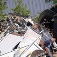 Pile of scrap metal and broken debris beside a corrugated metal wall outdoors