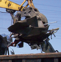 Yellow crane lifting a mangled dark metal object at a scrapyard