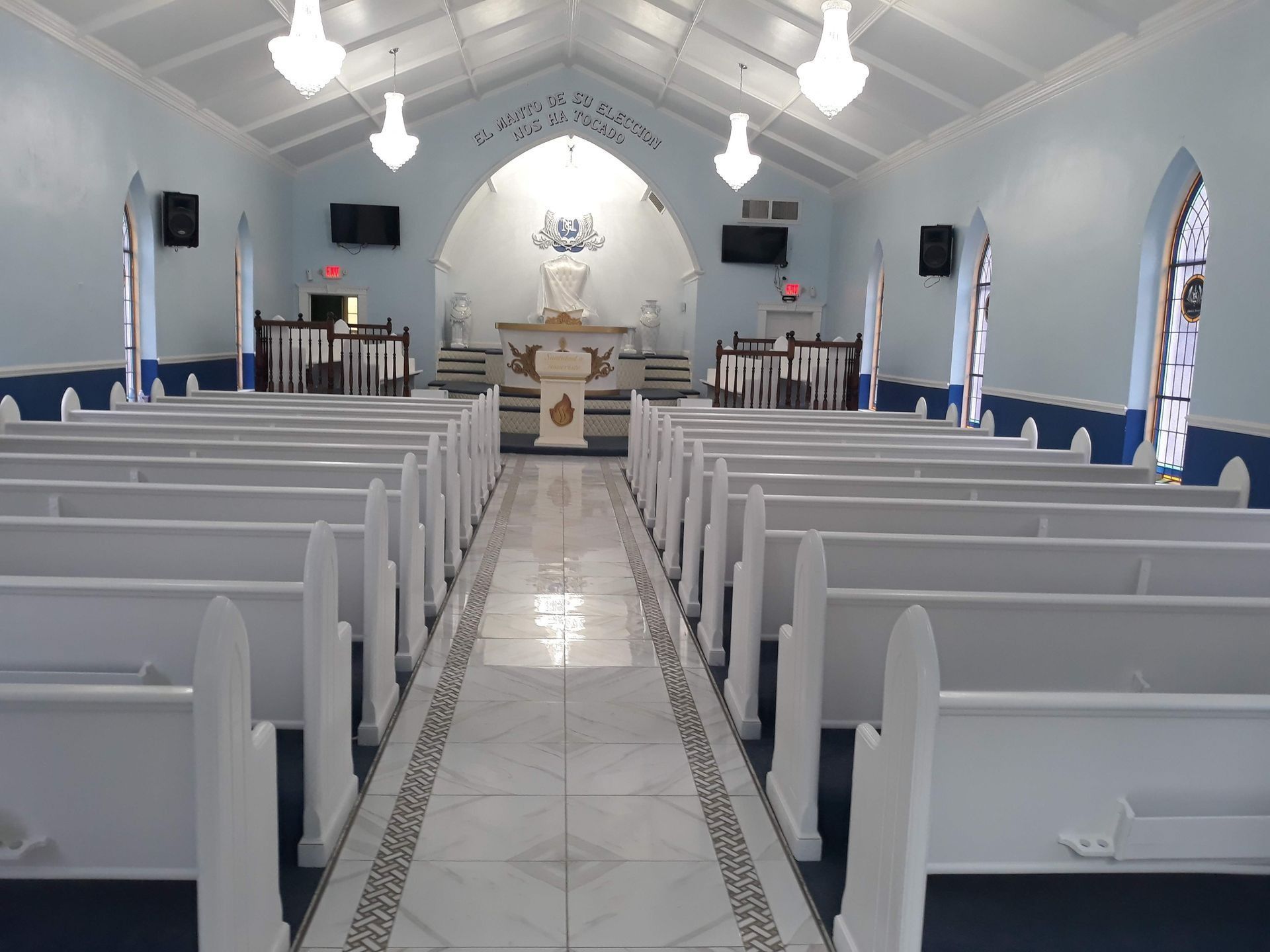 Interior of a light blue church with white pews and a central aisle leading to a raised altar area.