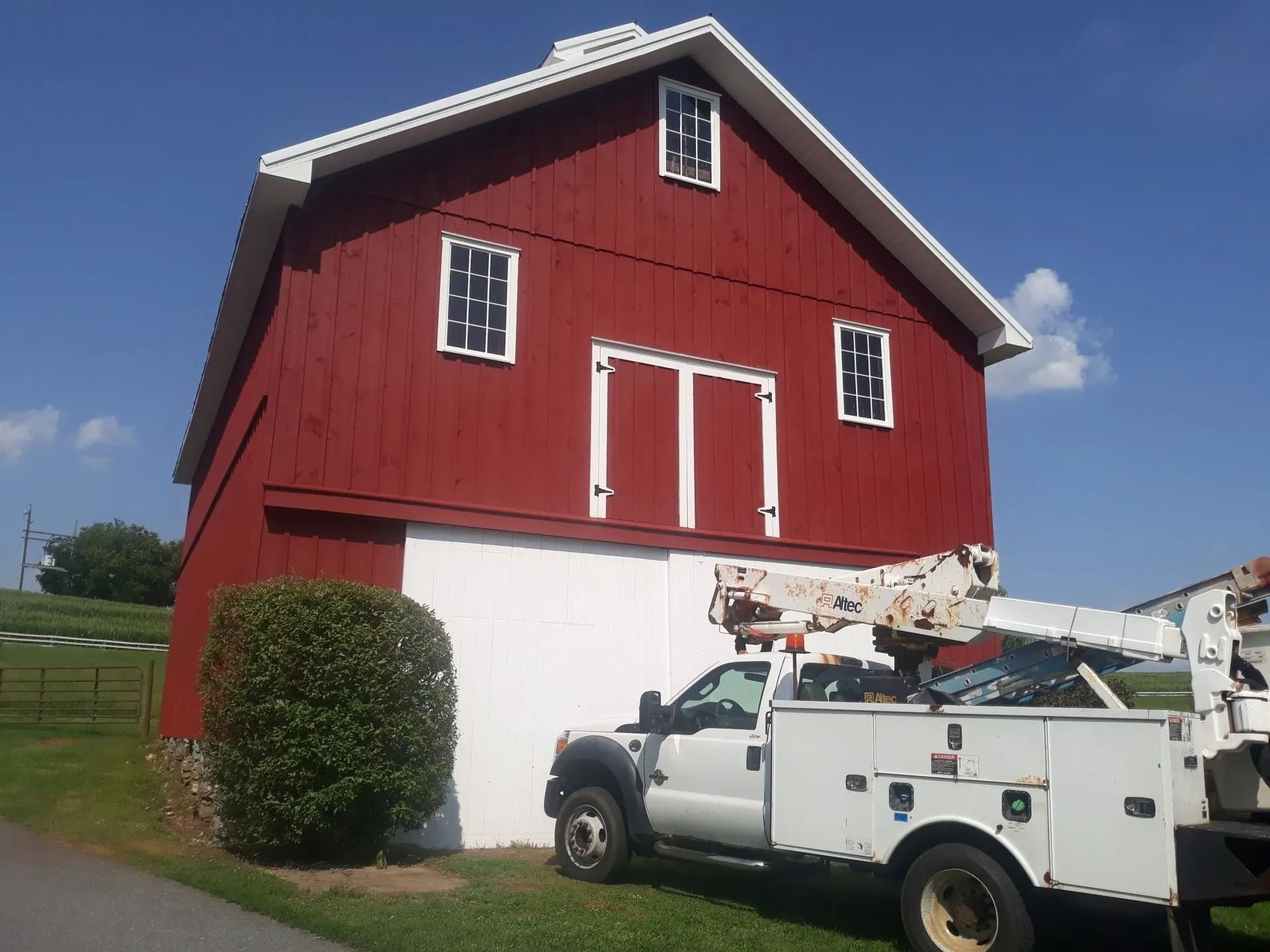 Red barn with white doors and trim; white truck with lift parked in front.