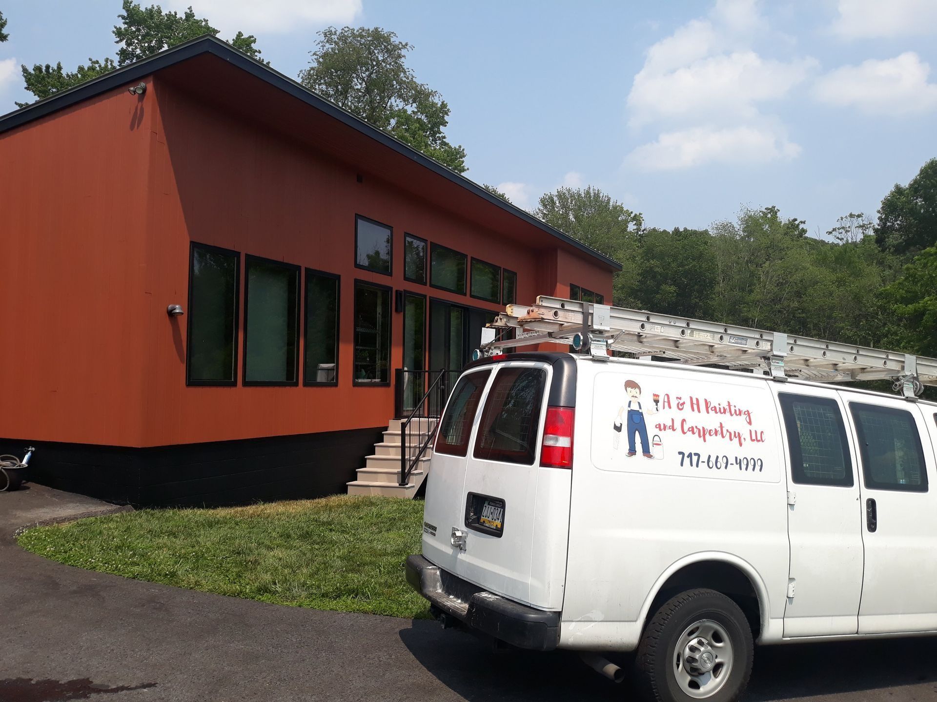 White van with ladder parked in front of a modern orange house.