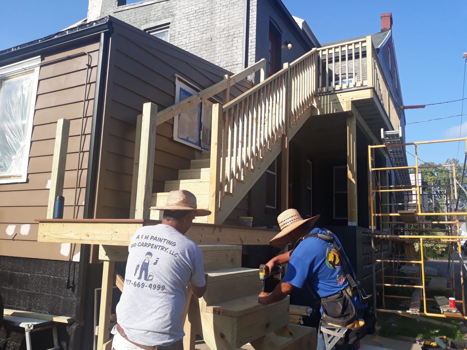 Two workers constructing wooden stairs and deck on a house exterior.