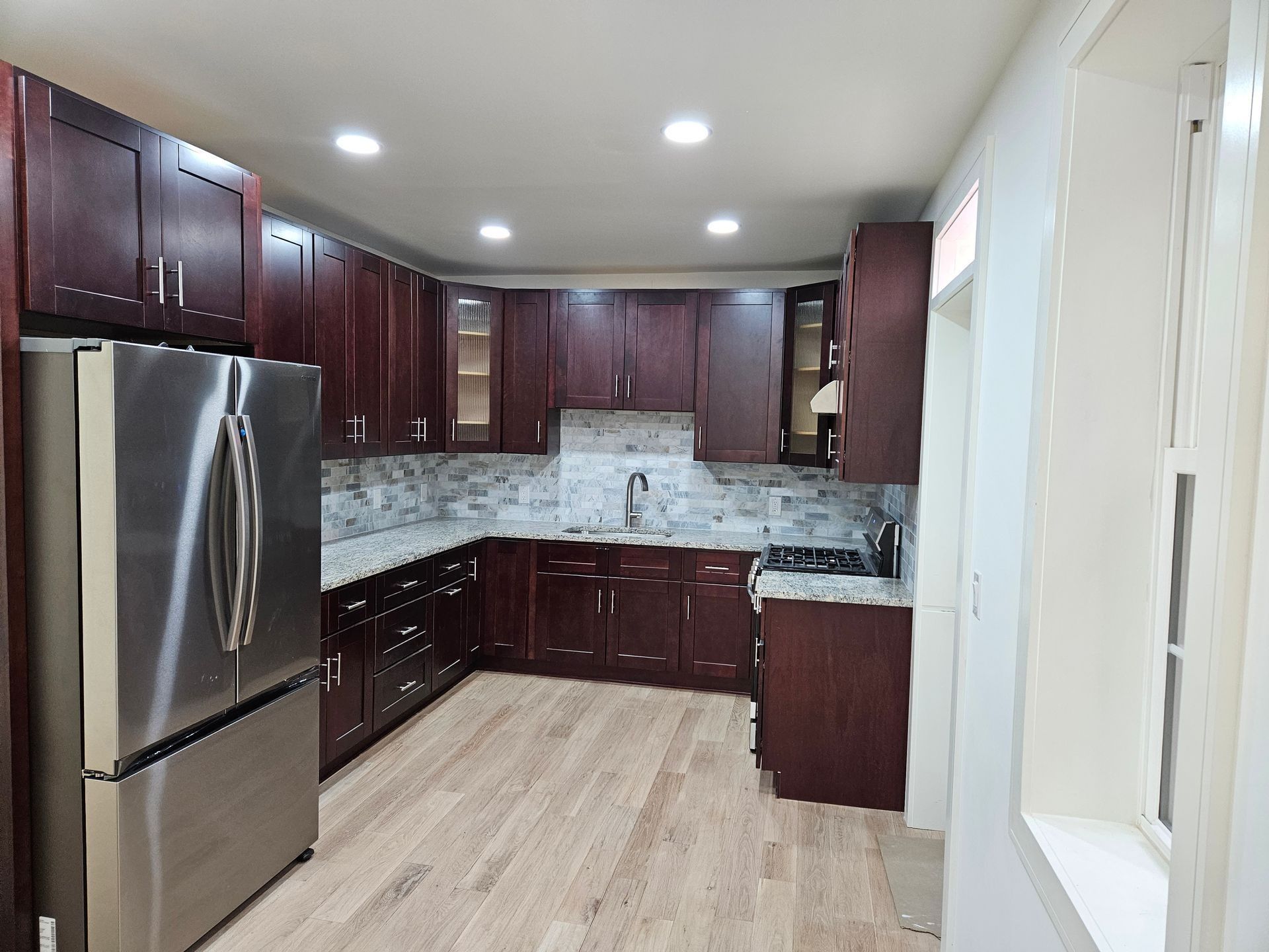 Kitchen with dark wood cabinets, stainless steel refrigerator, granite countertops, and light wood floor.