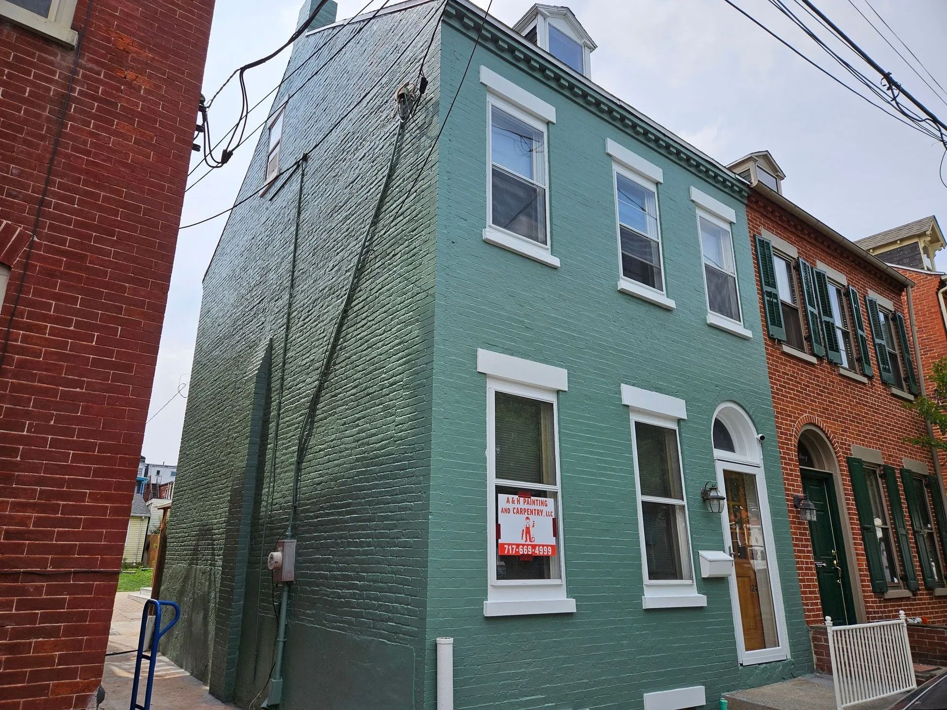 Green brick house with white trim, three windows on top, two on the bottom, and a door.