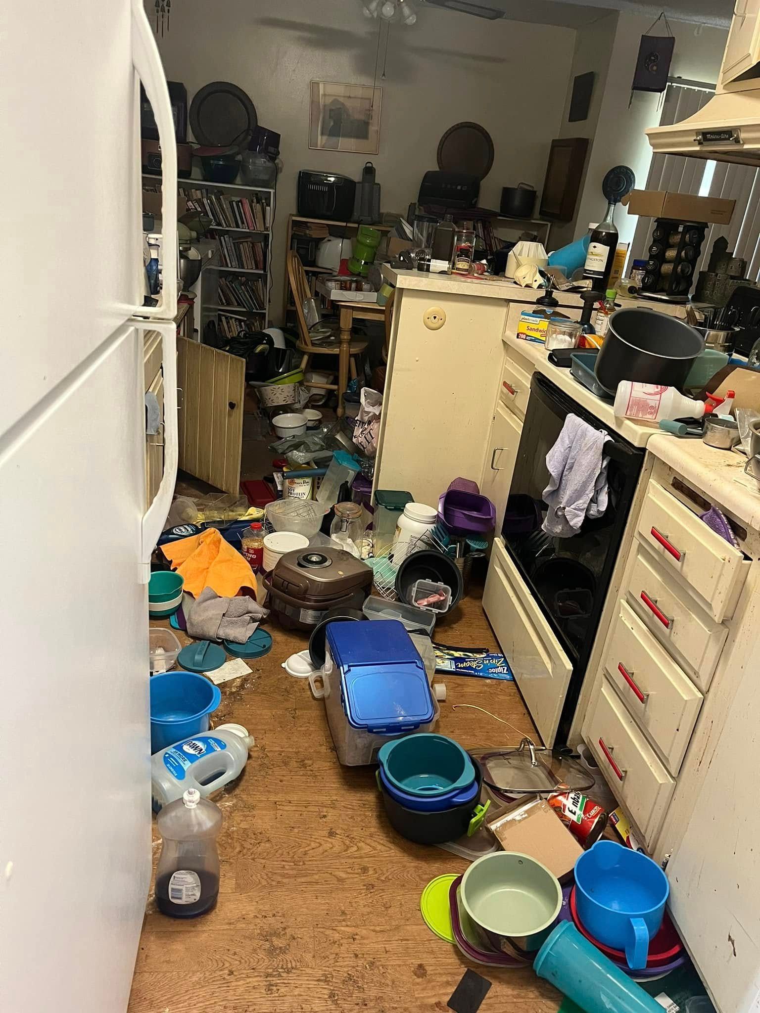 Cluttered kitchen with trash and objects covering the floor, counters, and appliances.