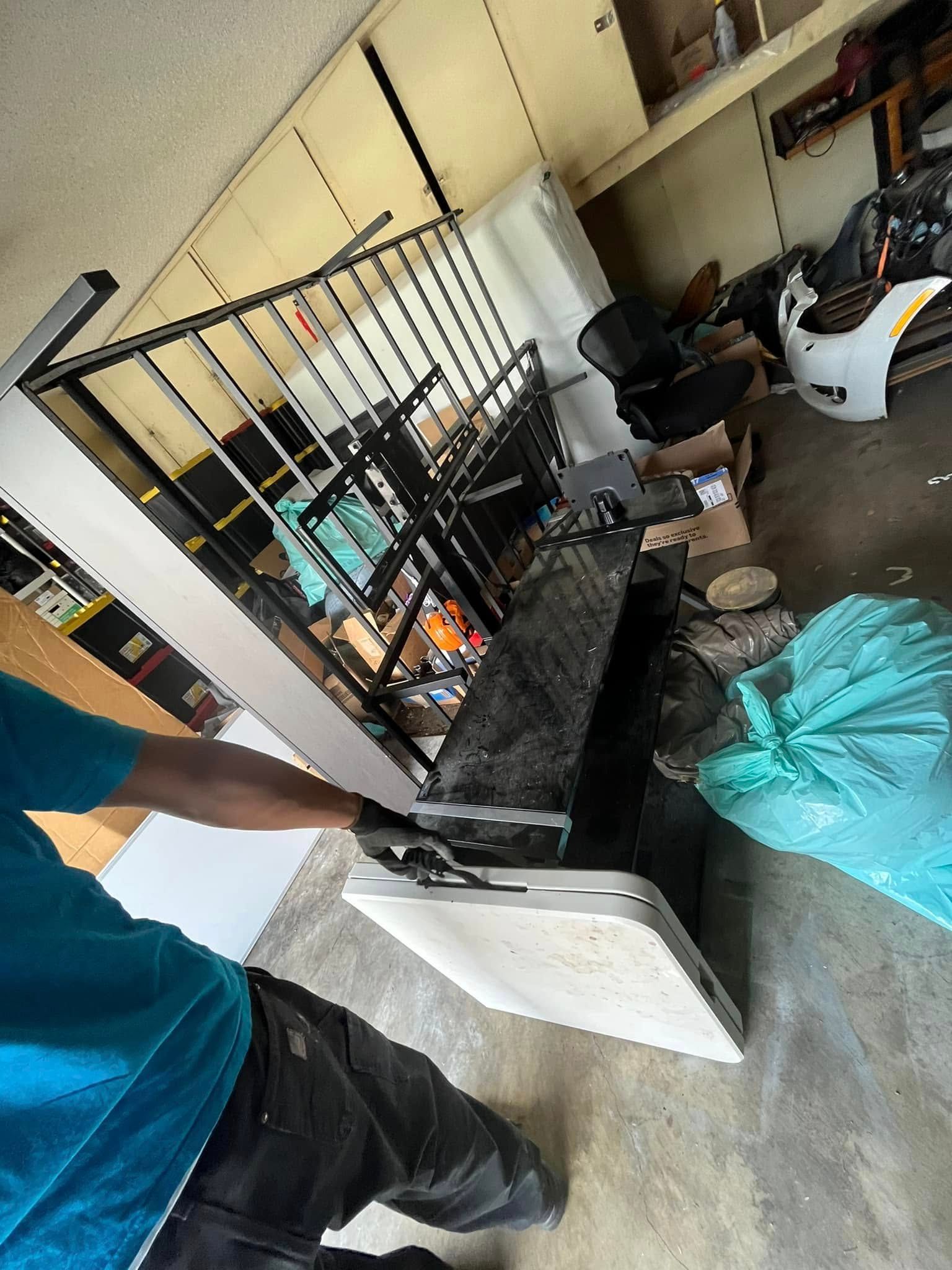 A person in a blue shirt and dark pants handles a table, next to a black metal shelf in a garage setting.