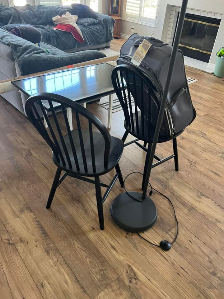 Two black Windsor chairs and a black floor lamp on a wood floor. A gray couch and TV are in the background.