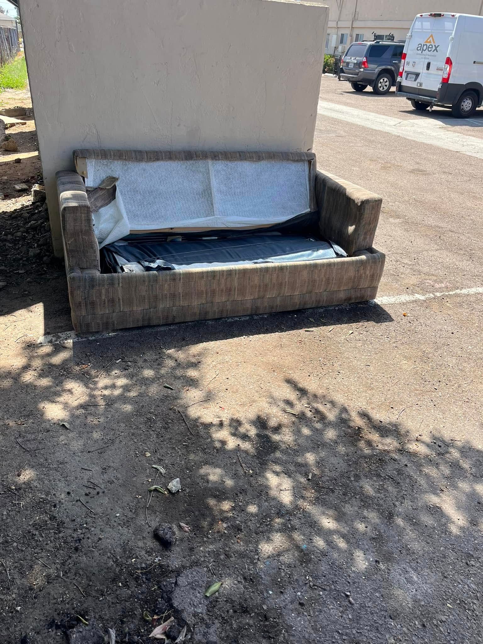 A worn concrete bench against a light-colored wall. The seat has tattered fabric and is surrounded by a gravel lot.