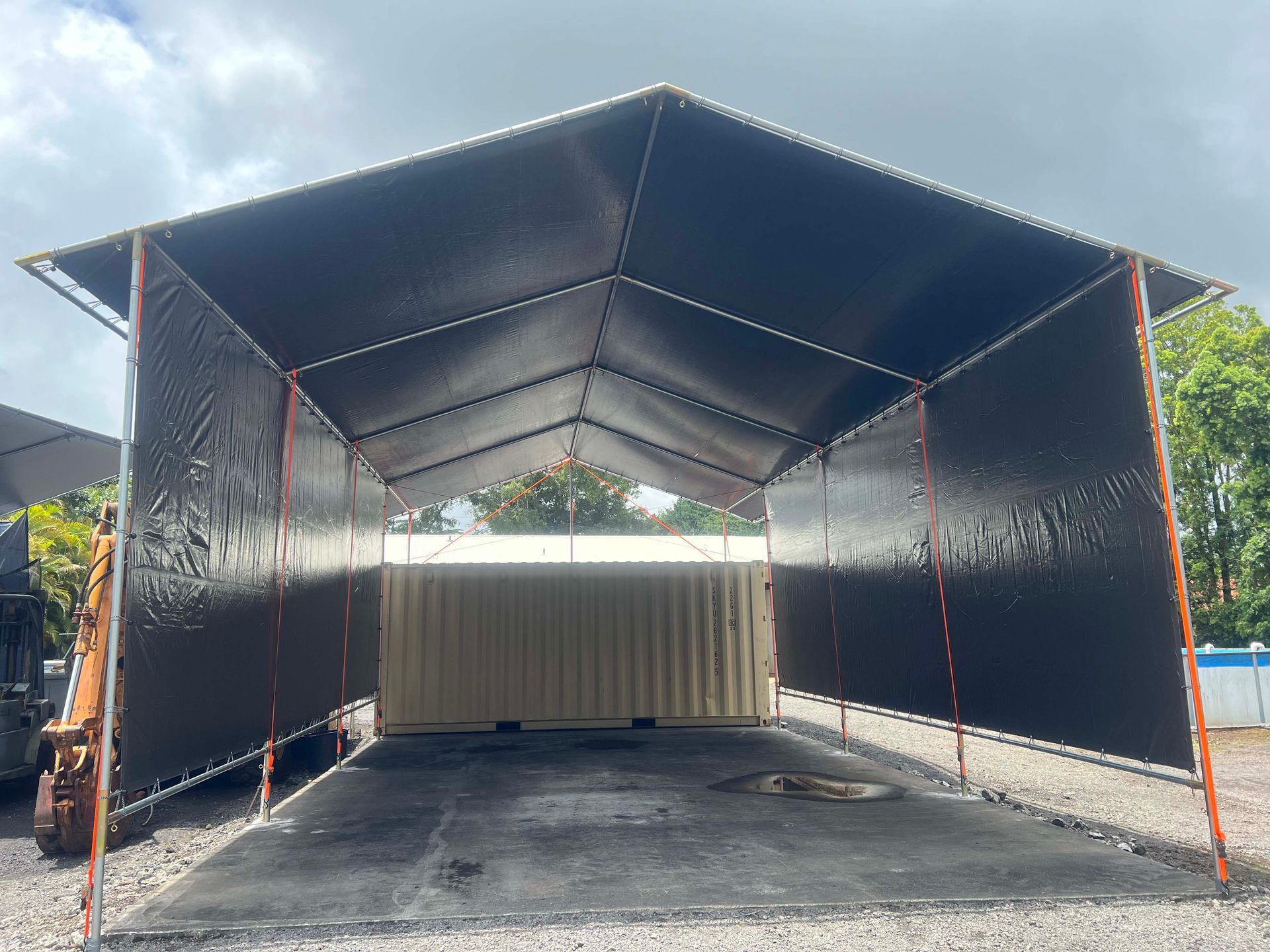 A large black tent is sitting on top of a gravel lot.