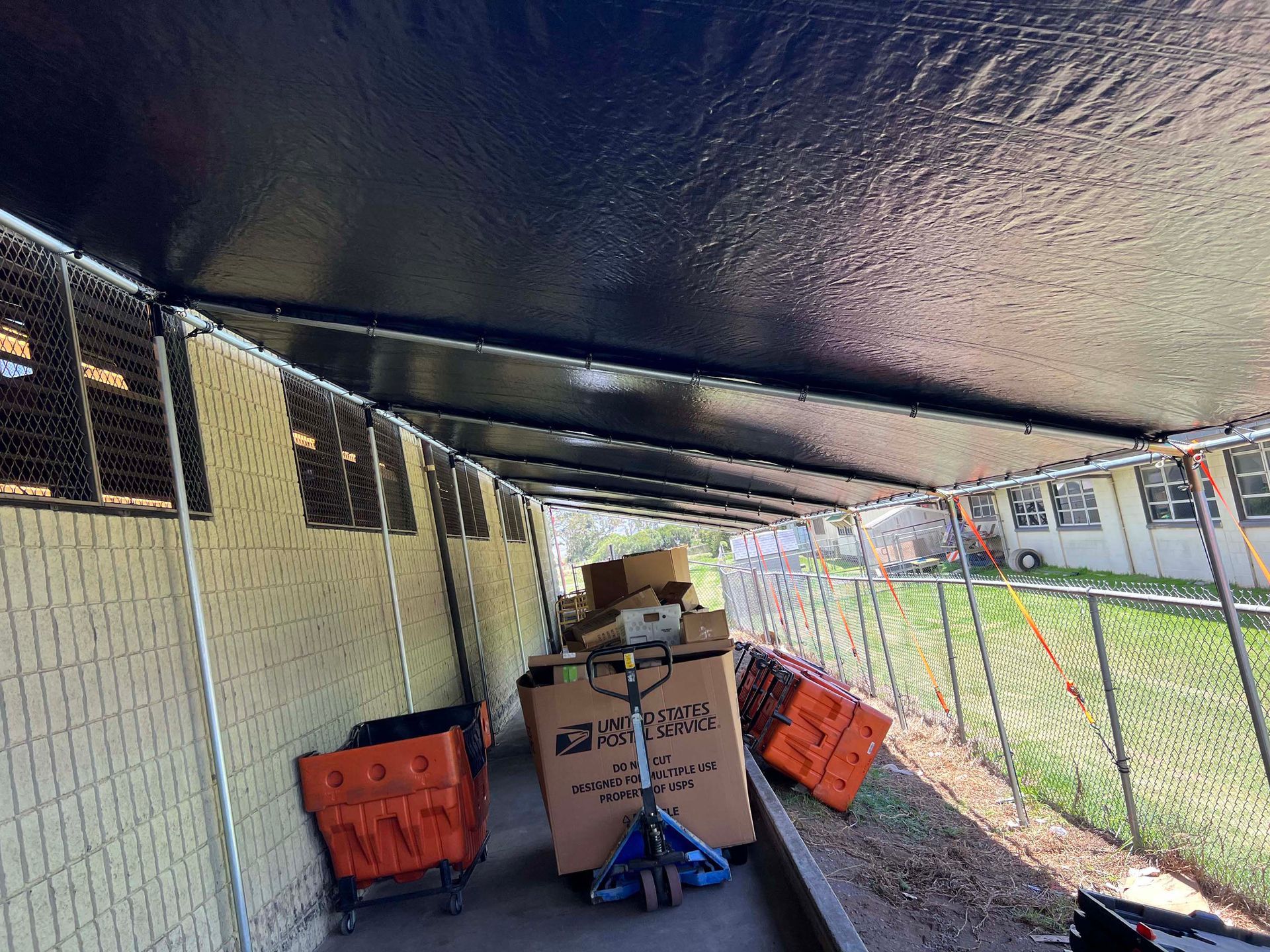 A fenced in area with boxes on the ground under a canopy.