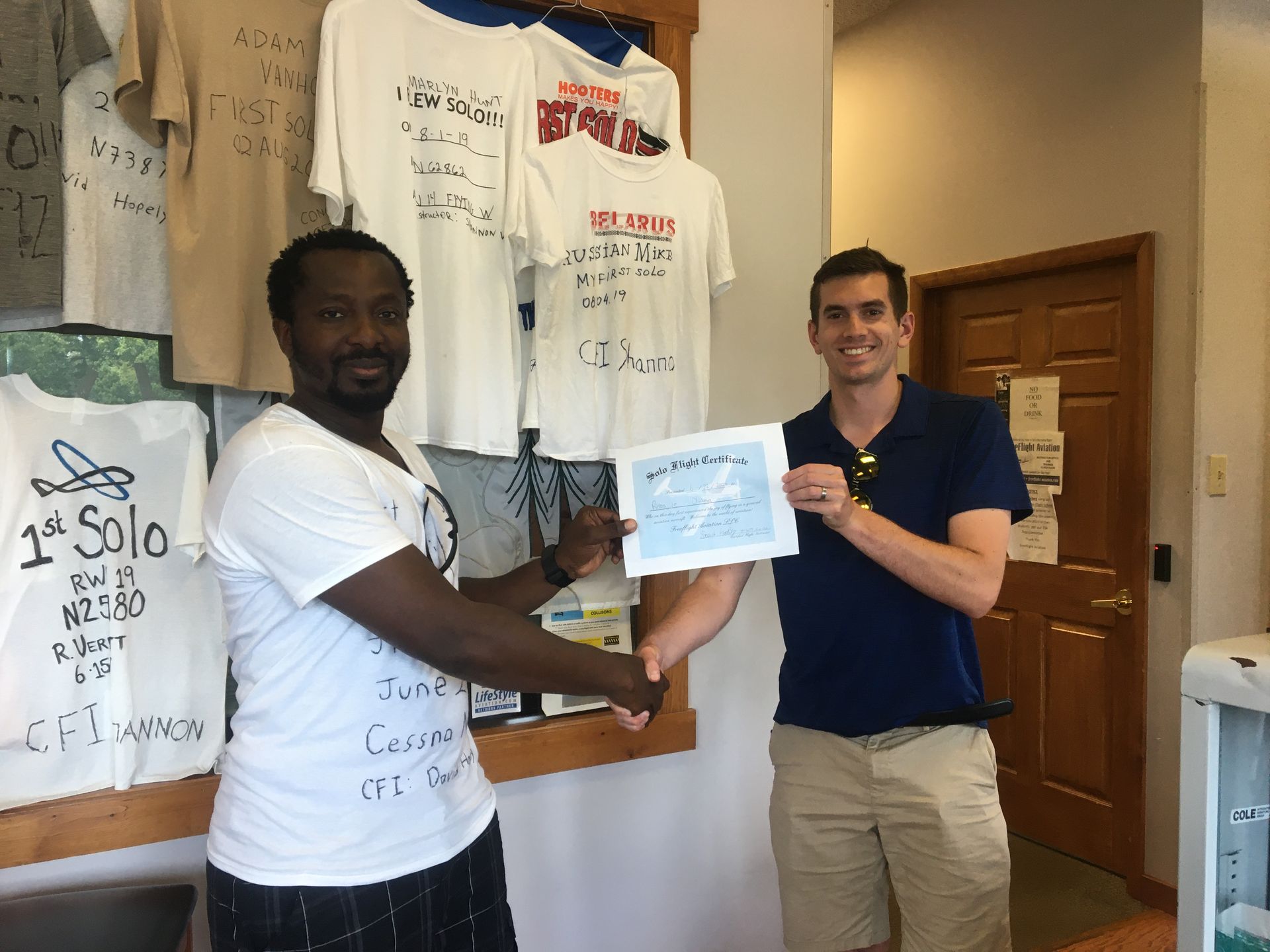 two men shaking hands in front of a display of shirts