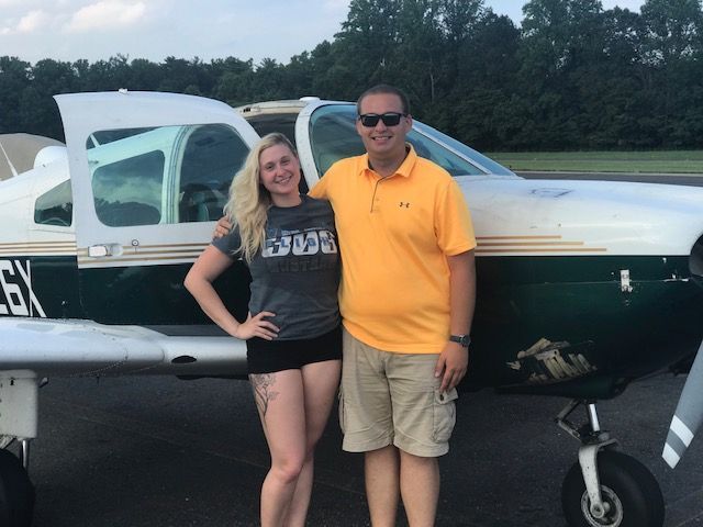 a man and a woman standing in front of a plane with the number 6x on it