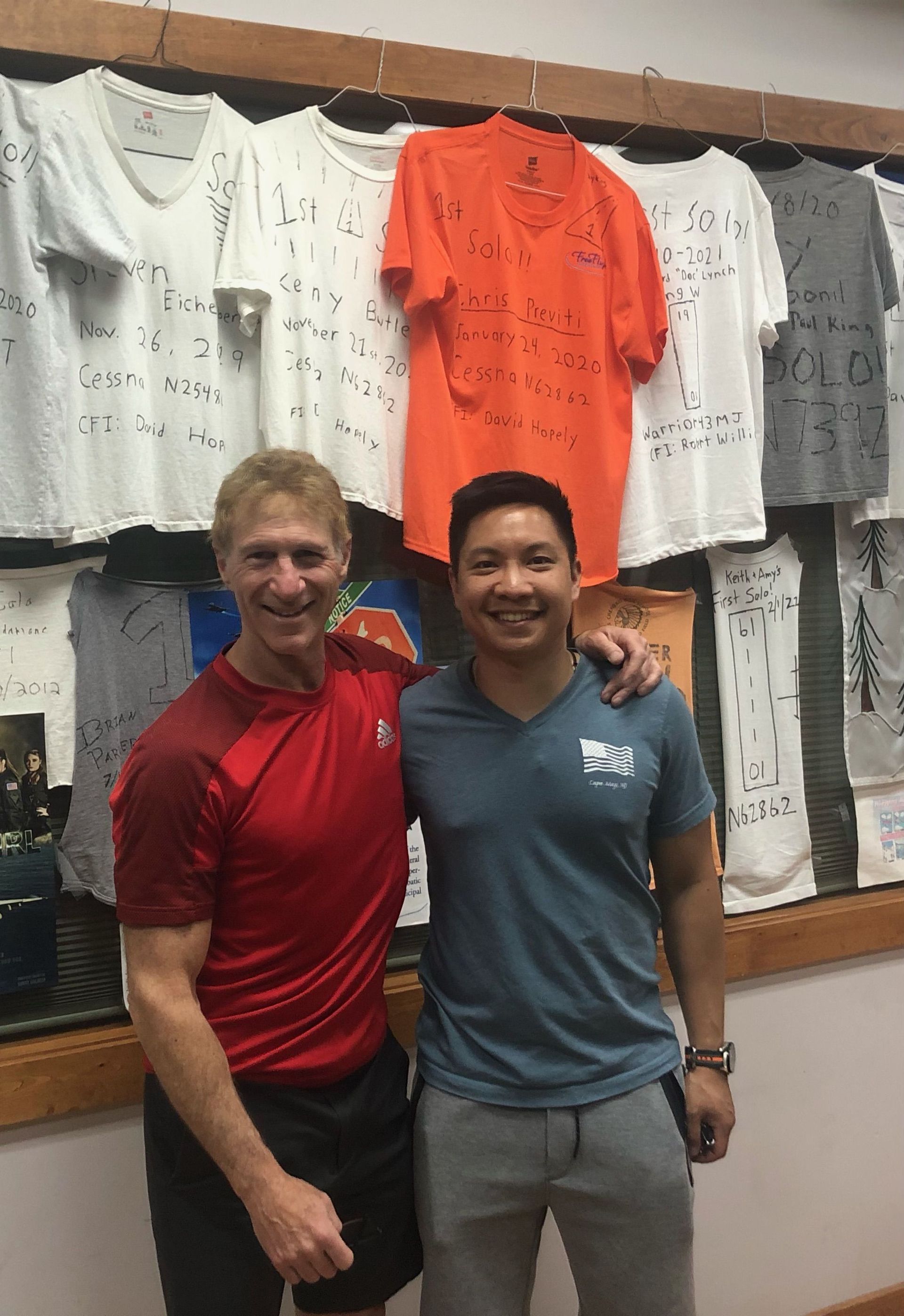 two men are posing for a picture in front of a wall with shirts hanging on it