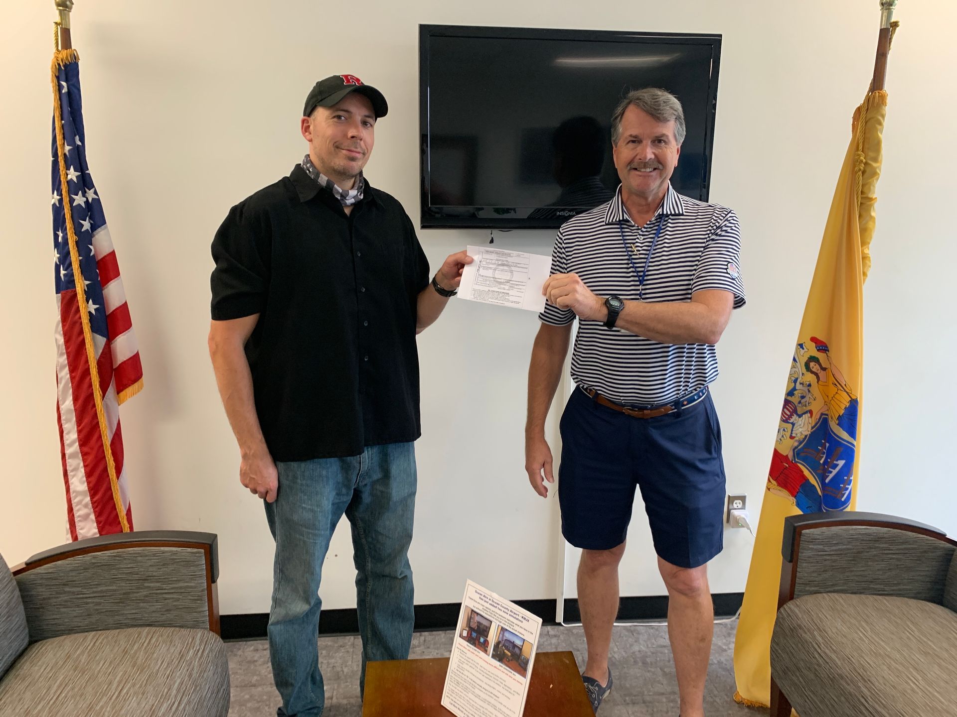 two men are standing next to each other in a living room holding a check