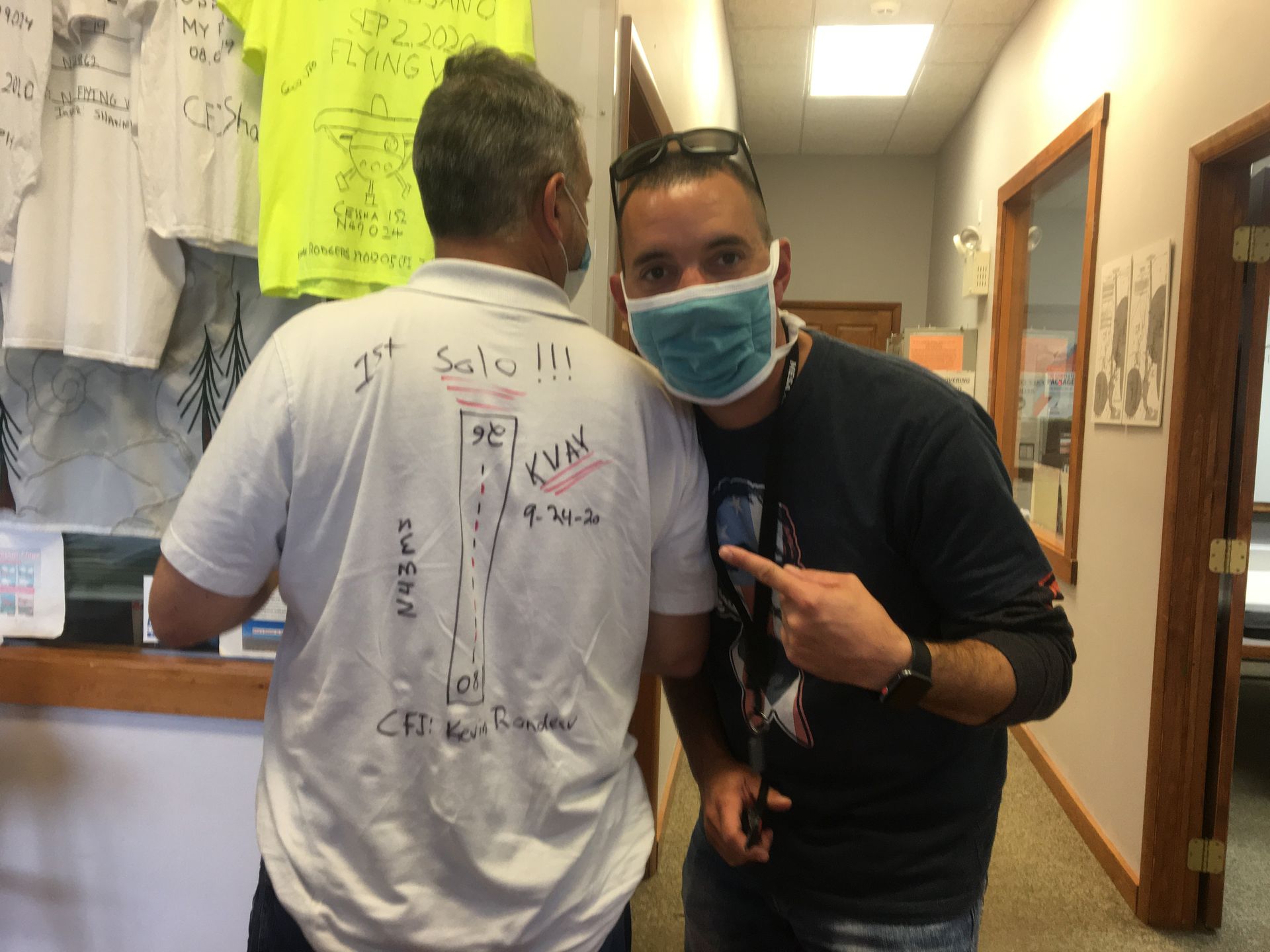 a man wearing a mask is pointing at the back of another man 's shirt