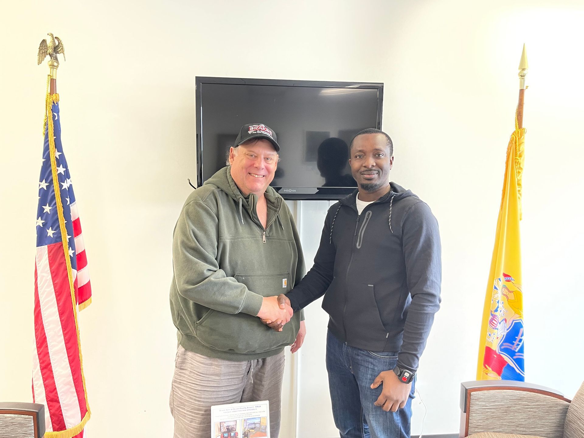 two men are shaking hands in front of an american flag in a room