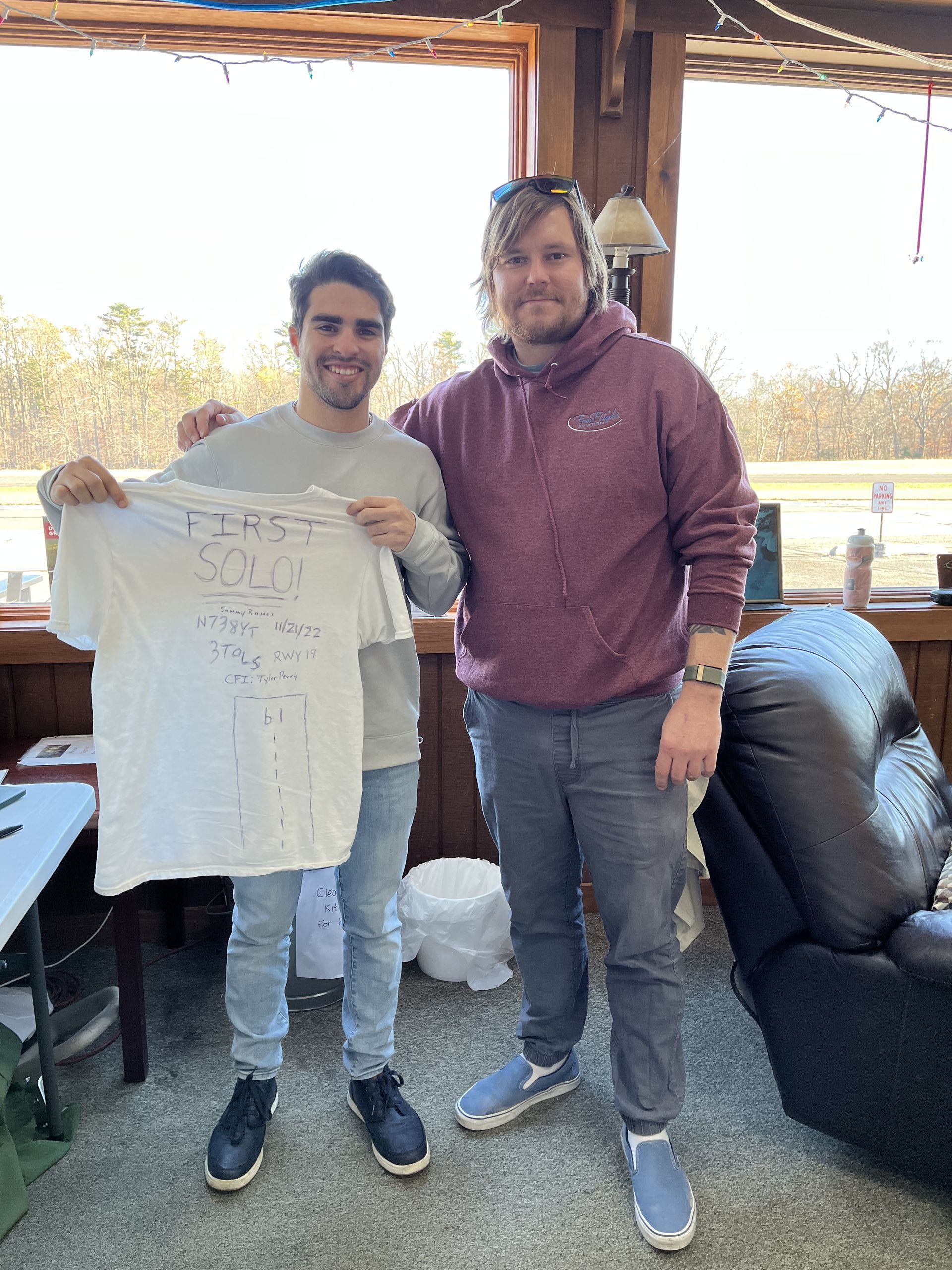 two men are standing next to each other in a living room holding a white t-shirt