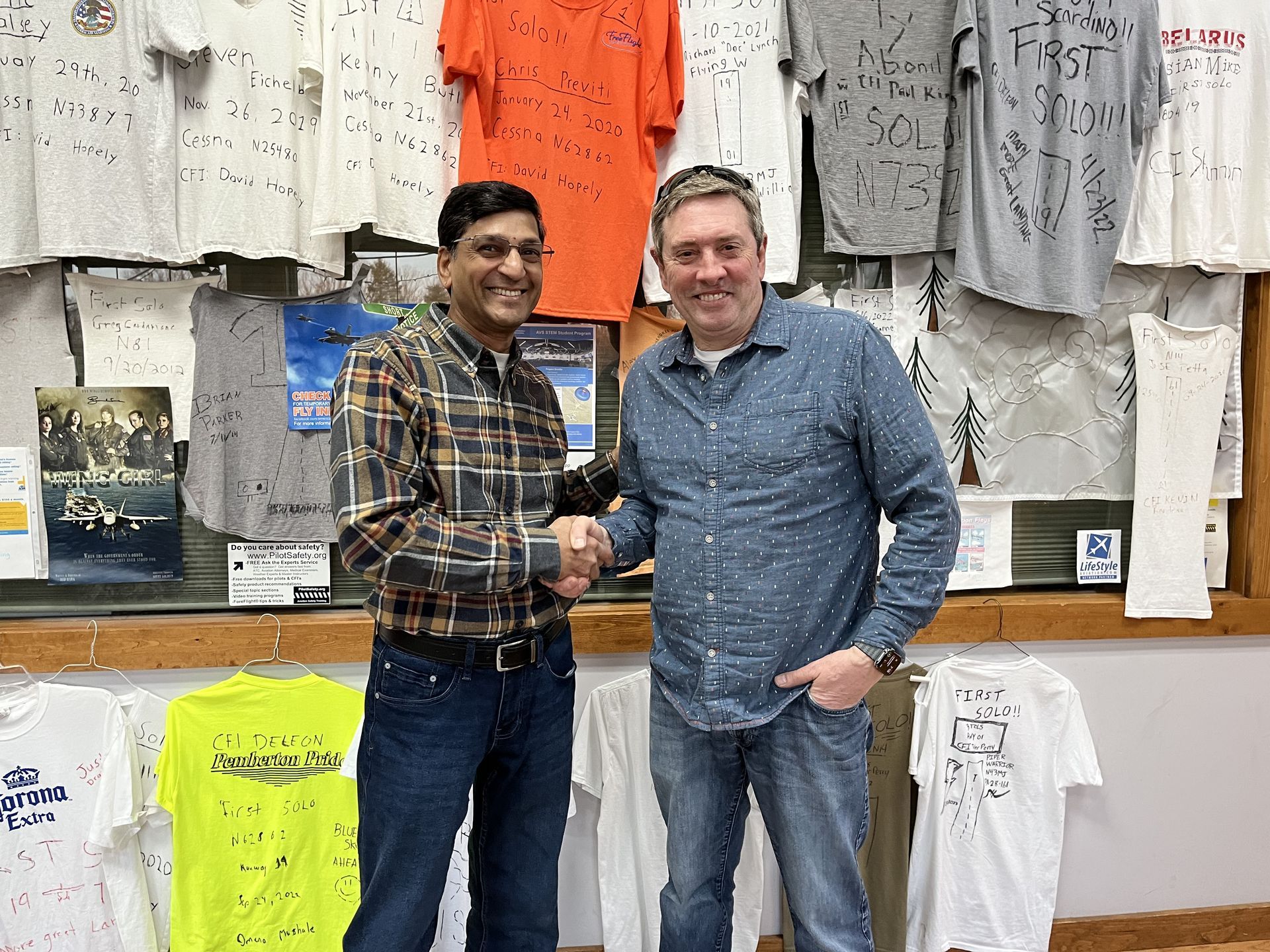 two men shaking hands in front of a wall of shirts