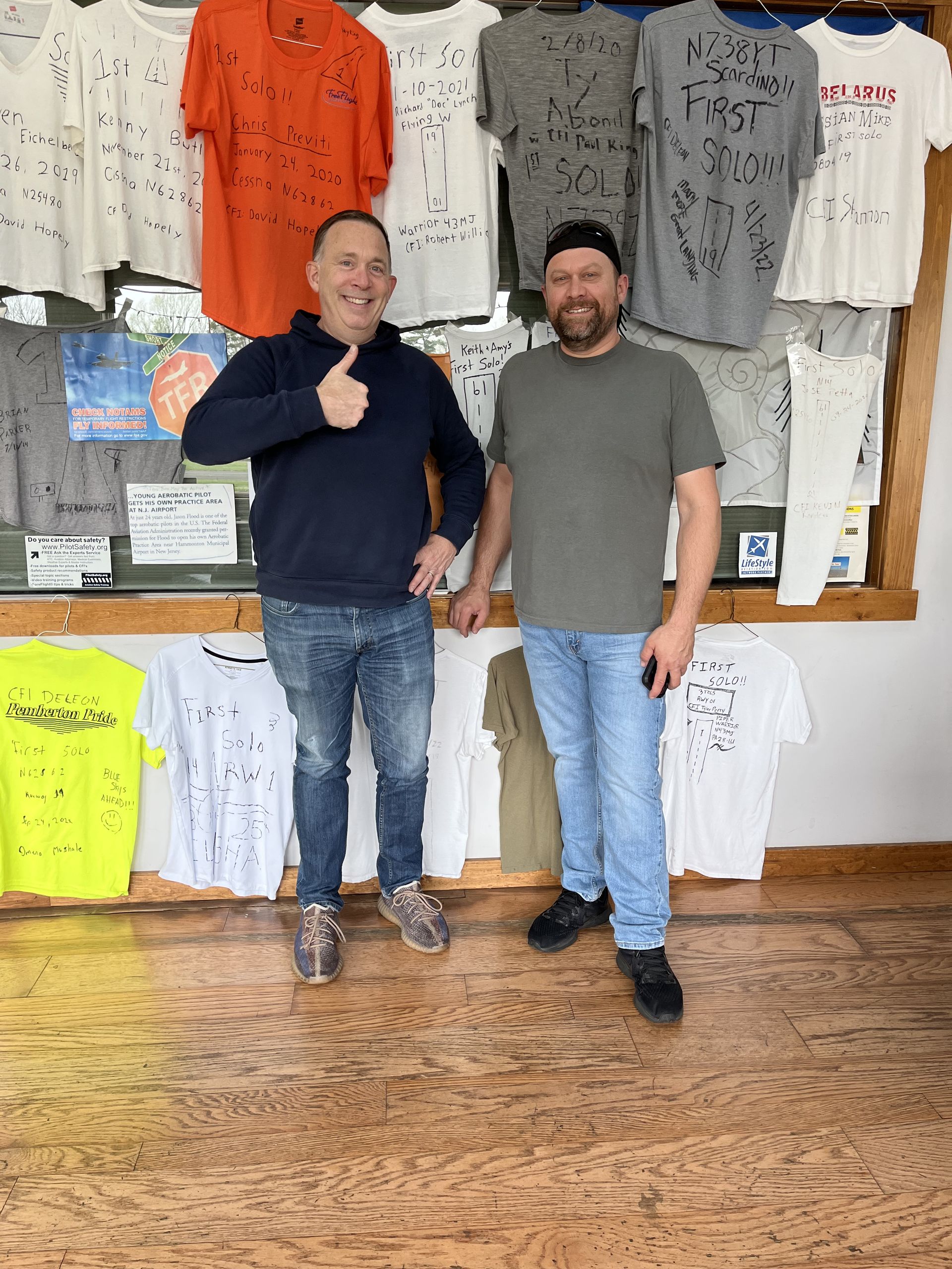 two men are standing in front of a display of t-shirts and one of them is giving a thumbs up