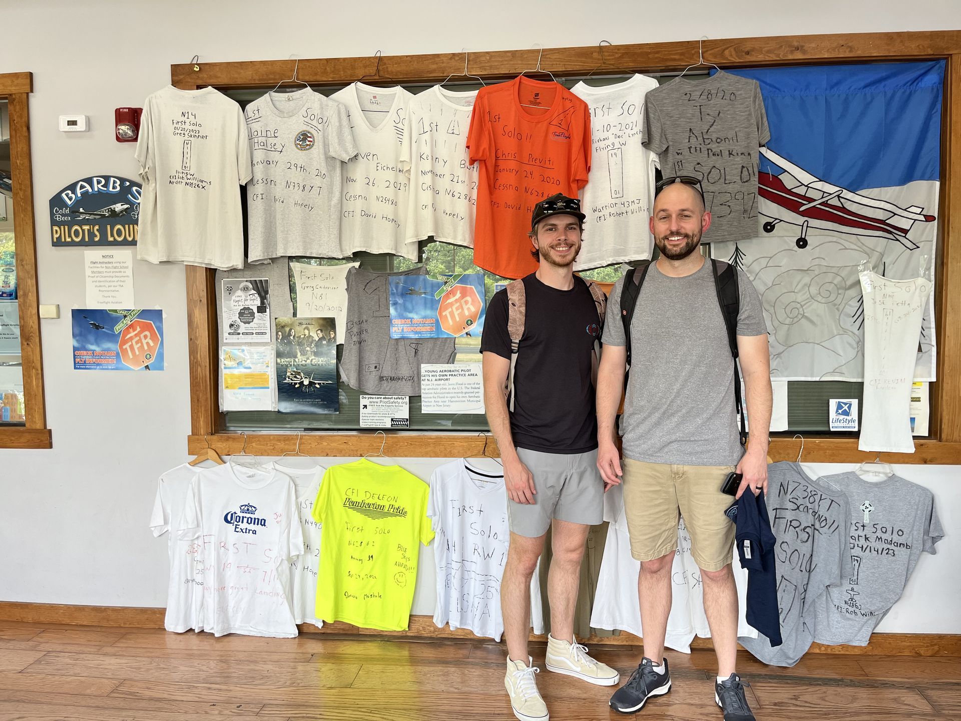 two men are standing in front of a wall with shirts hanging on it