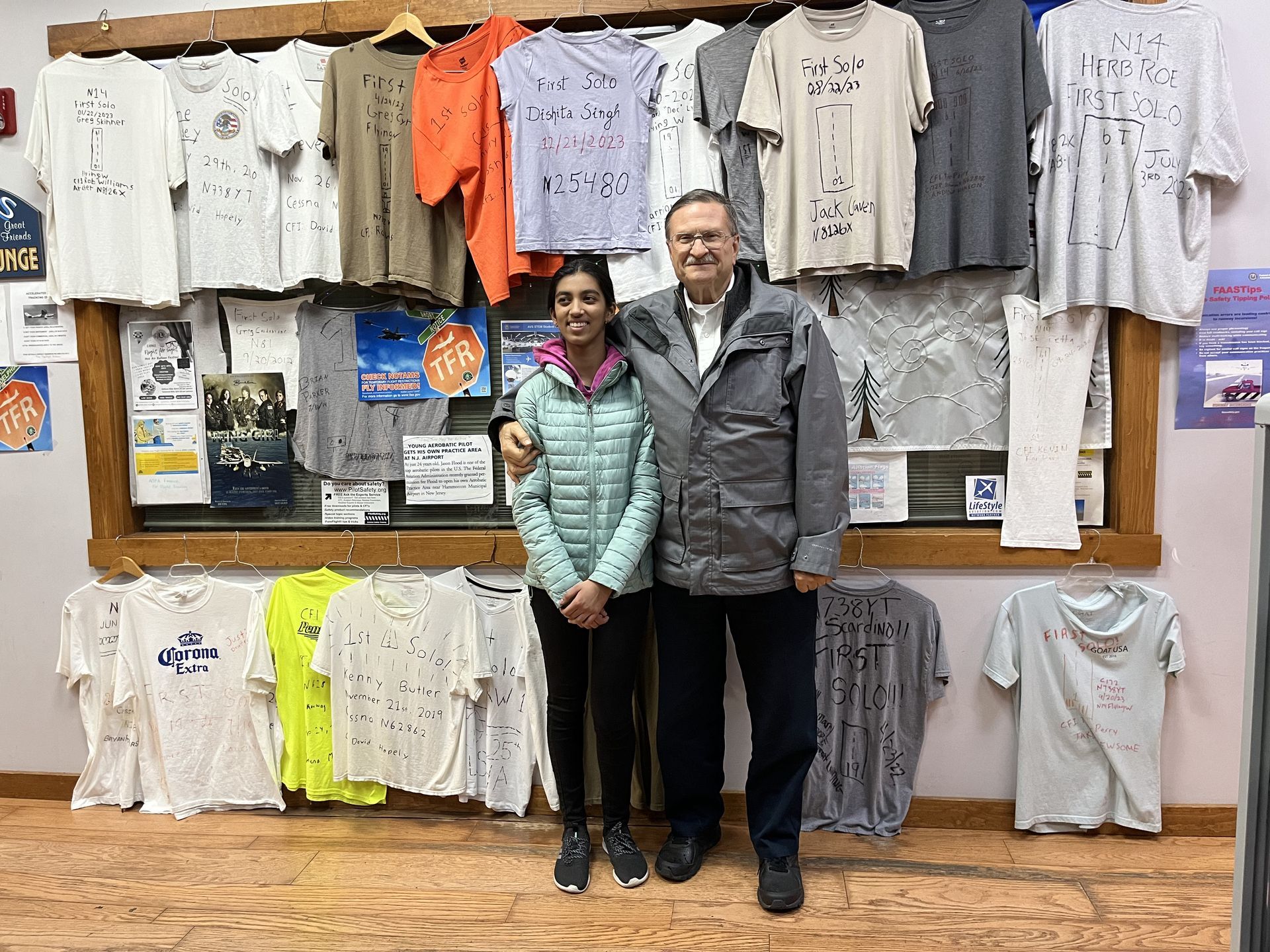 a man and a woman are standing in front of a wall of shirts