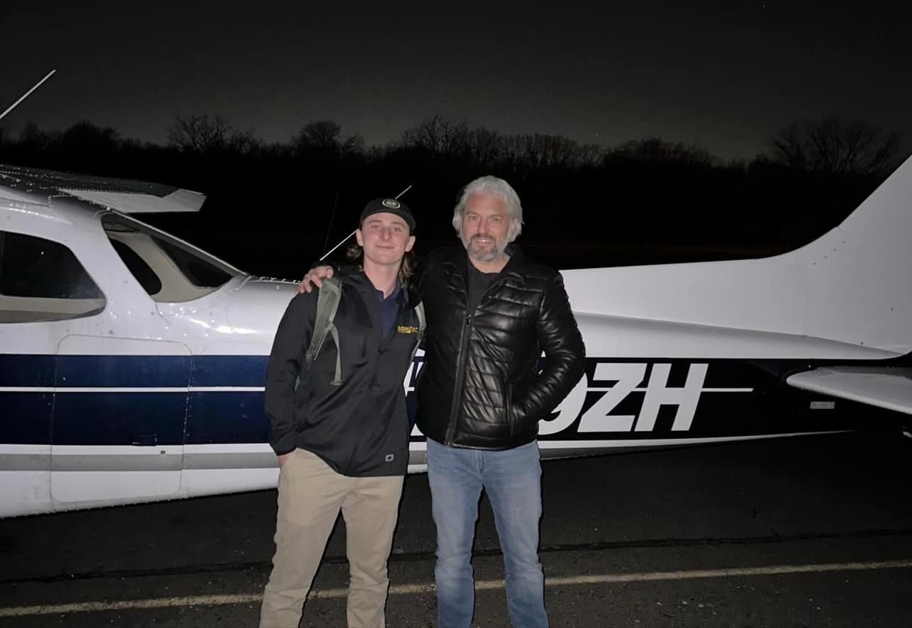 two men are posing for a picture in front of a plane that says jzh