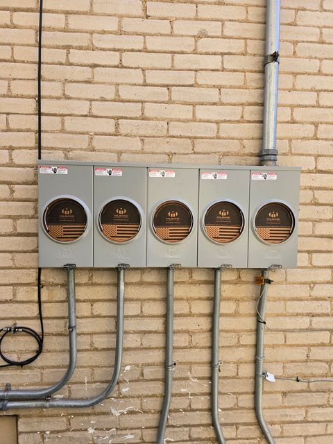 Five gray electrical meters mounted on a brick wall with conduit pipes.