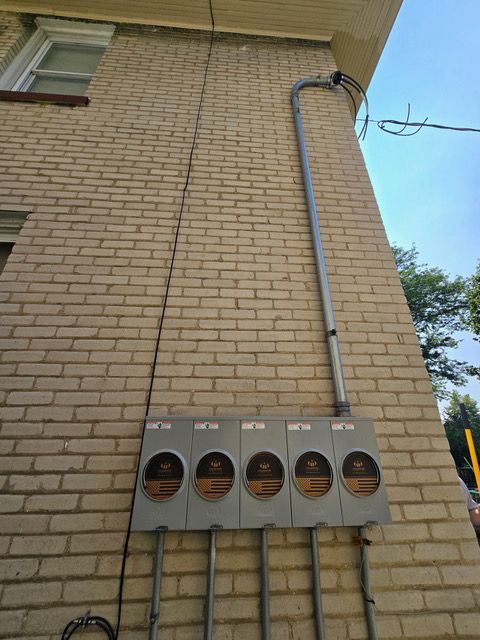 Five electric meters on a brick building exterior, with conduit running vertically.
