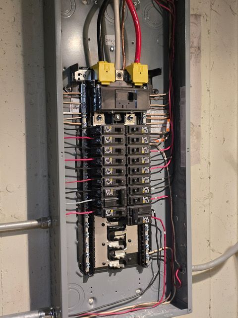 Electrical panel with various wires and circuit breakers. Gray metal box mounted on a wall.