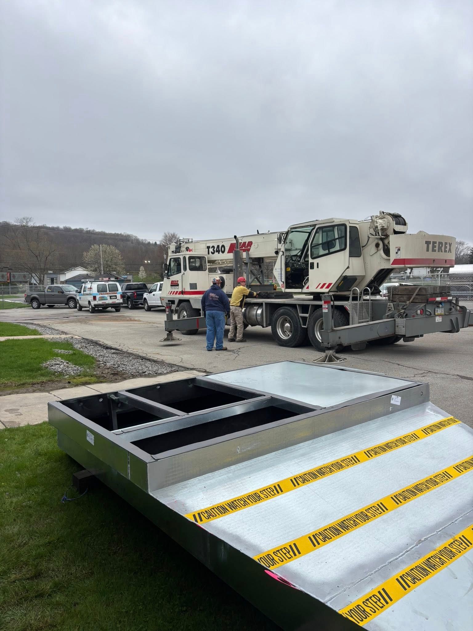A large crane with workers, a metal structure, and caution tape in a parking lot.