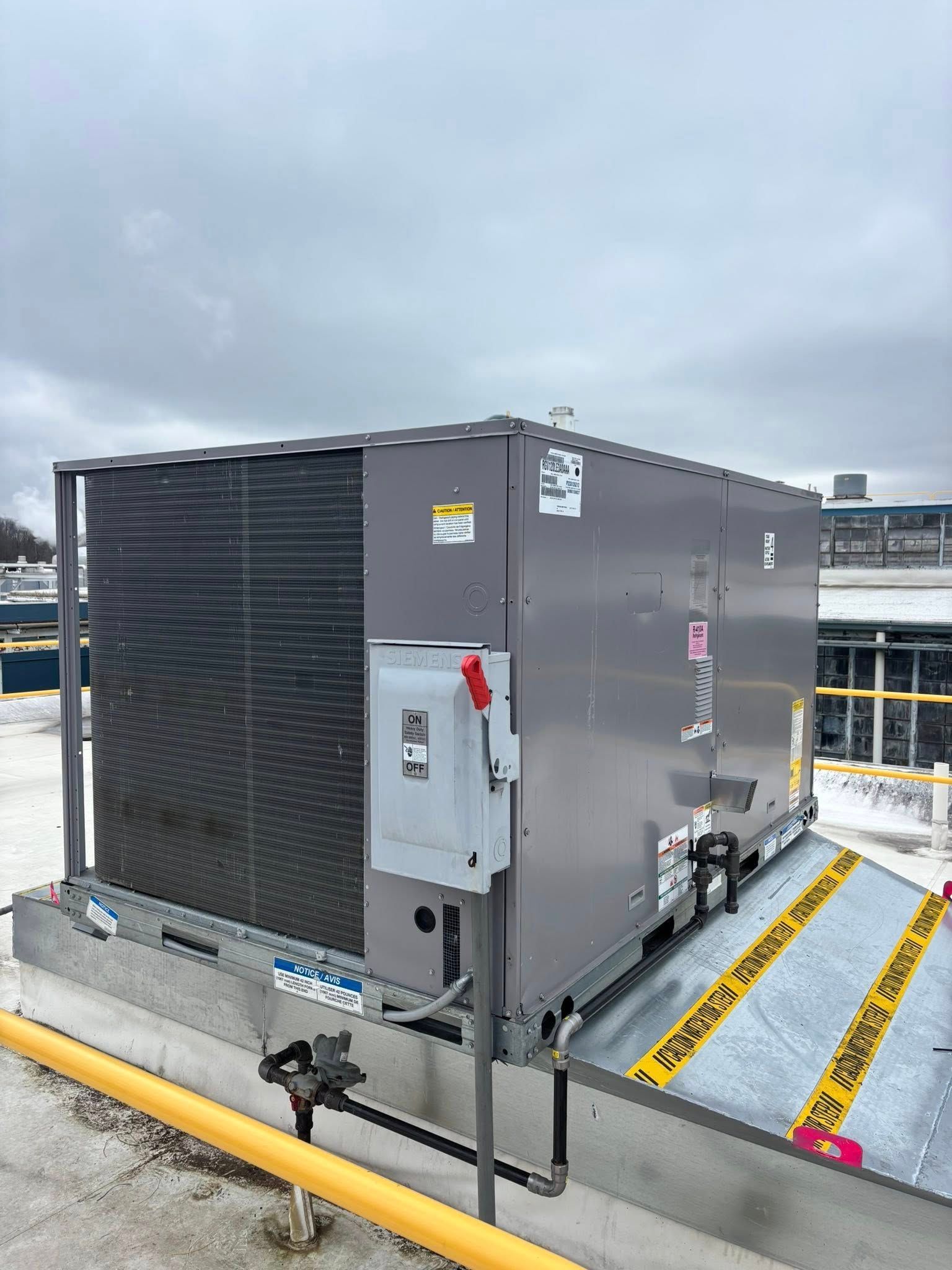 Gray HVAC unit on a rooftop, with a metal safety barrier and electrical box.