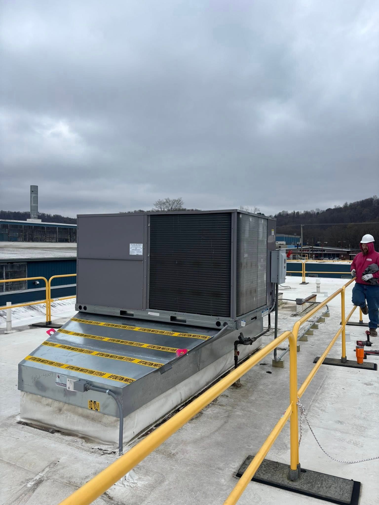 HVAC unit on a snowy rooftop with a worker in a hard hat.