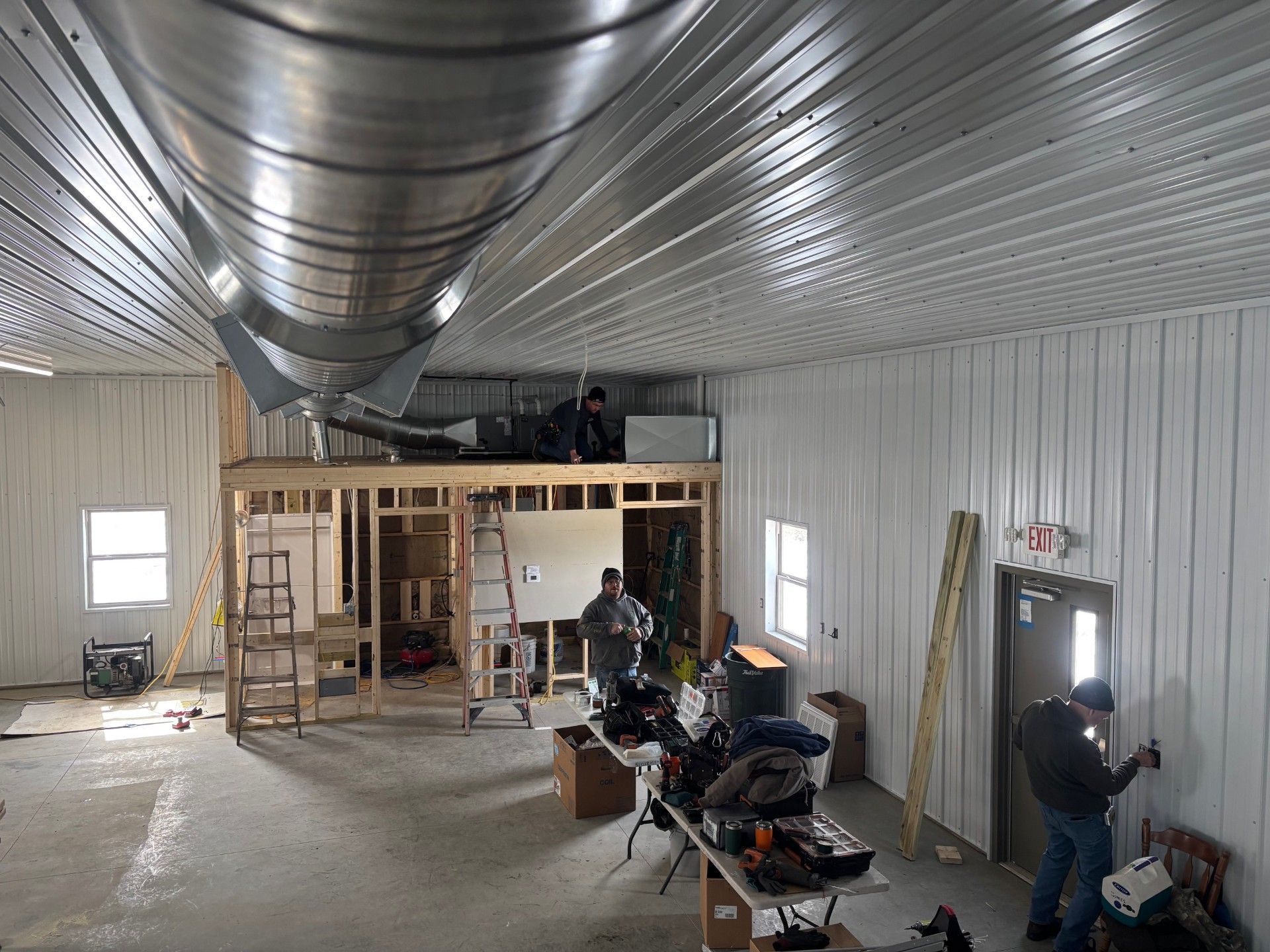 Interior of a construction site. Men working on walls, ceiling, and mezzanine level, tools and materials present.