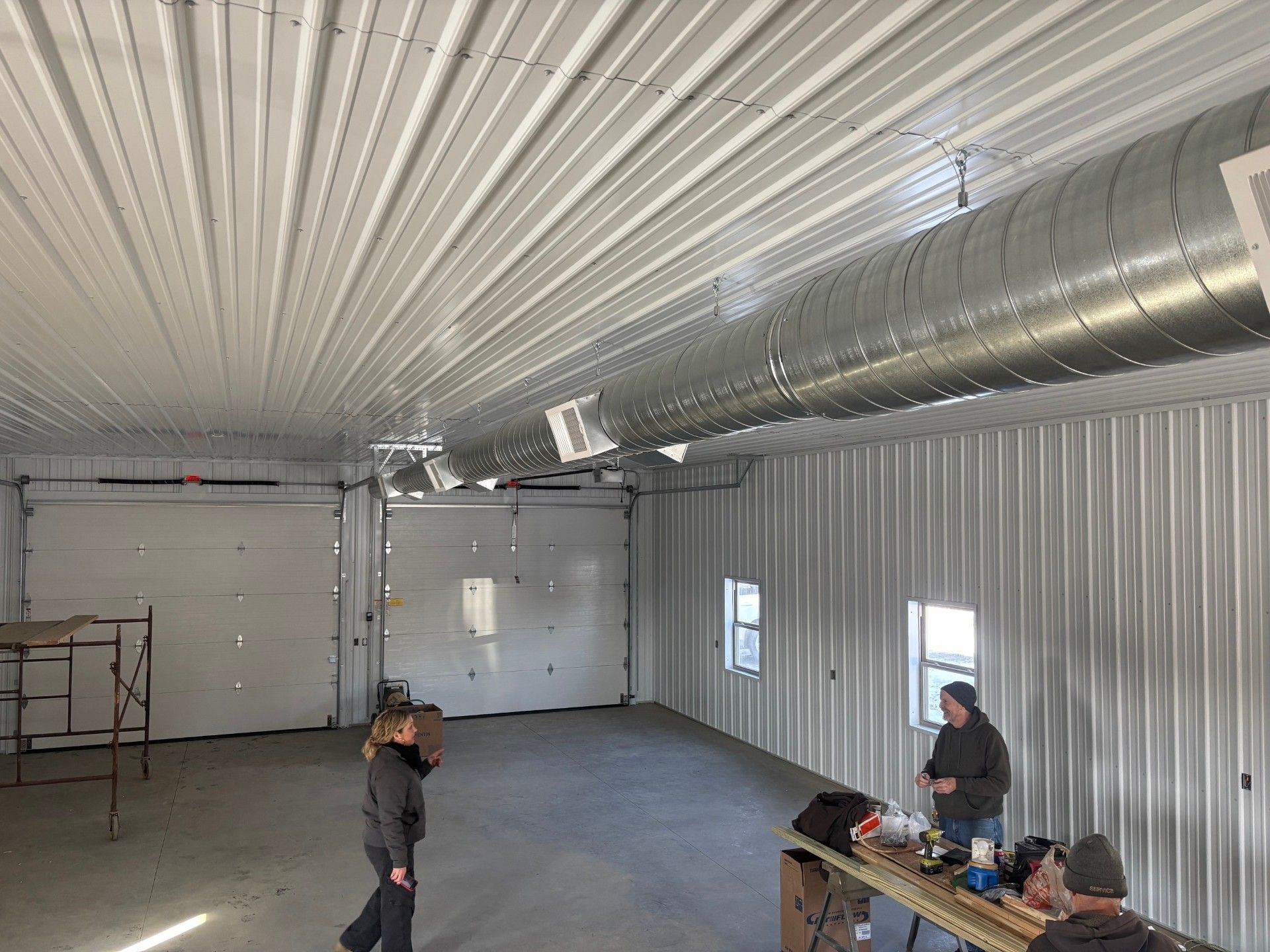 Interior of a metal building with people, garage doors, and ventilation ducts.
