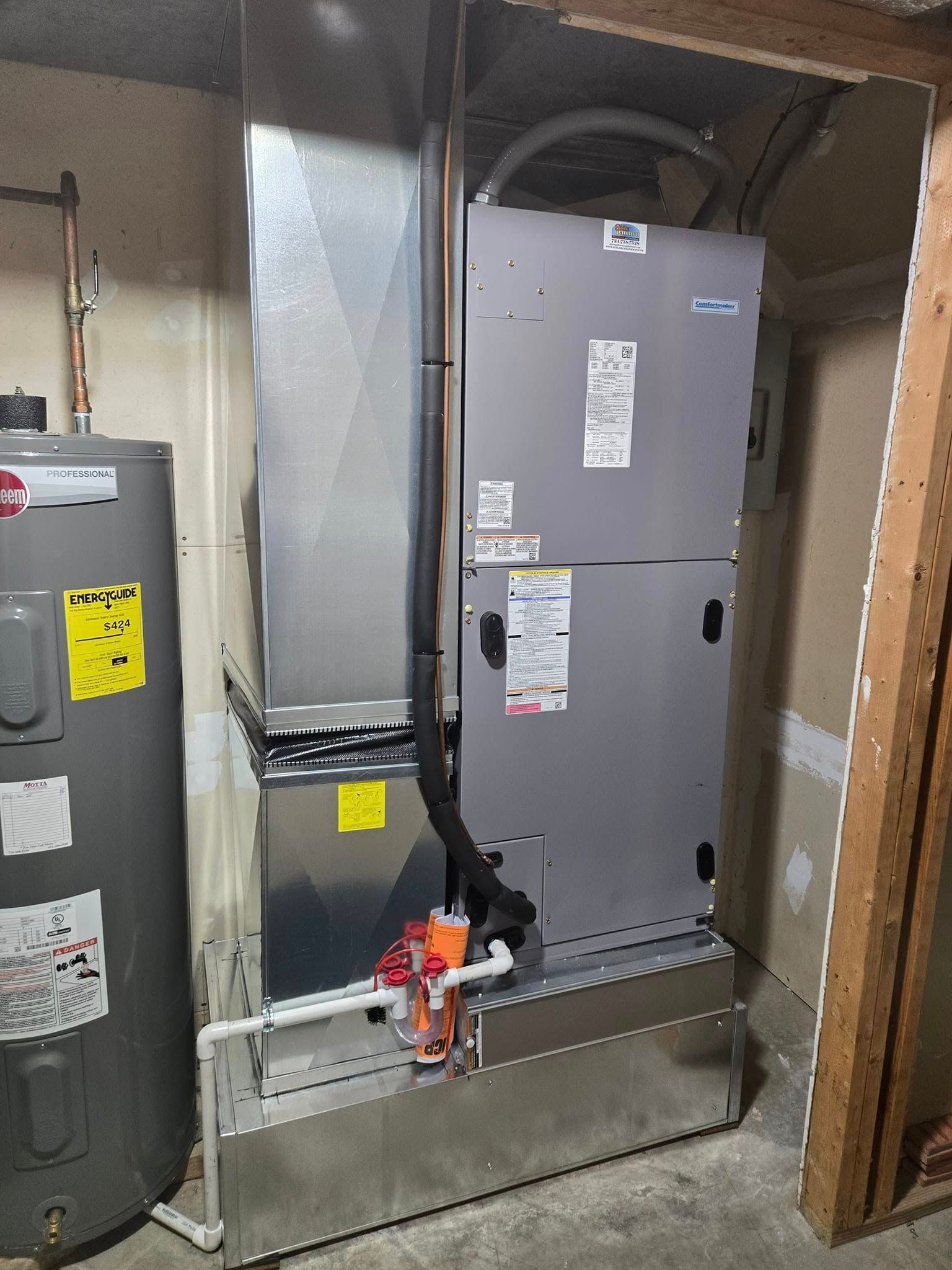 Water heater and HVAC unit in a utility room. Gray and silver appliances against beige walls.