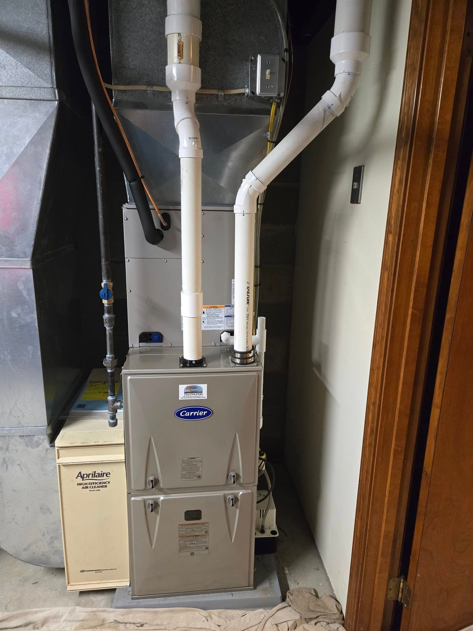 Furnace with white PVC pipes and ductwork in a basement setting.