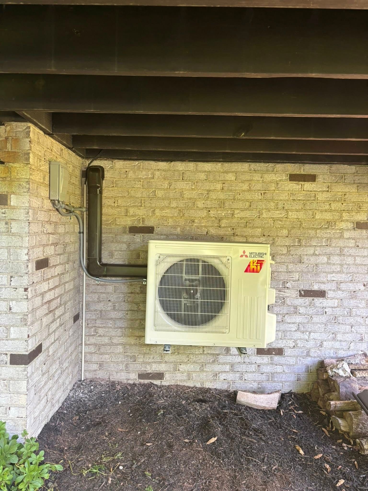 Exterior air conditioning unit mounted on a brick wall with exposed piping.