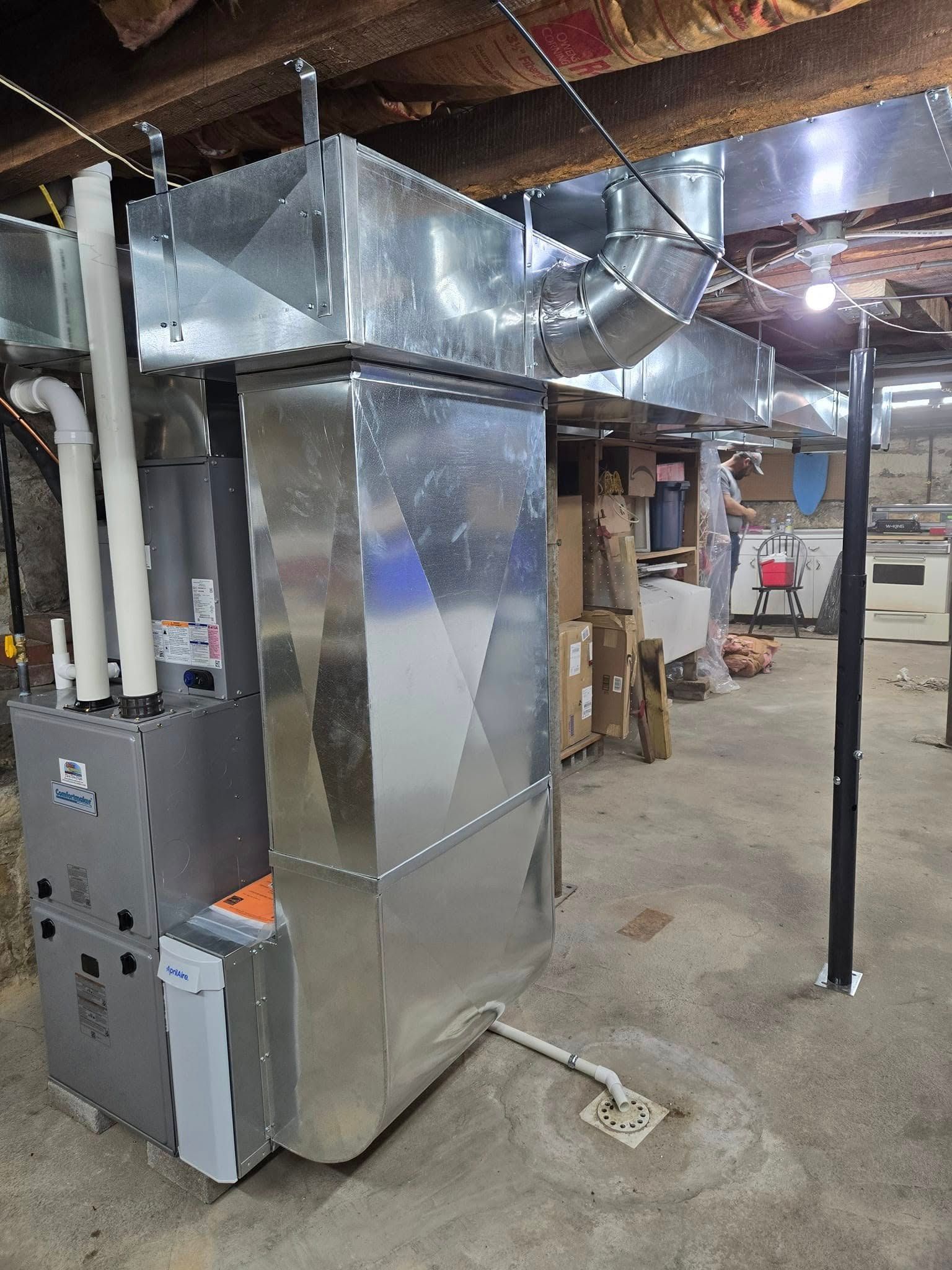Furnace with ductwork in a basement setting; a silver metal box, pipes, and metal vents.