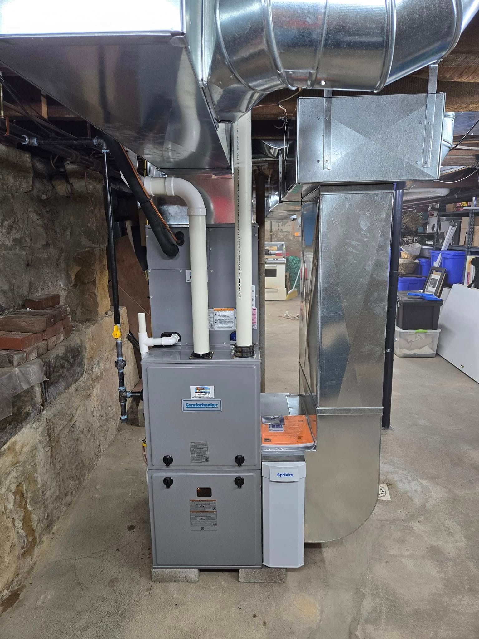 A new HVAC system in a basement with metal ducts and vent pipes. The unit is gray and white.