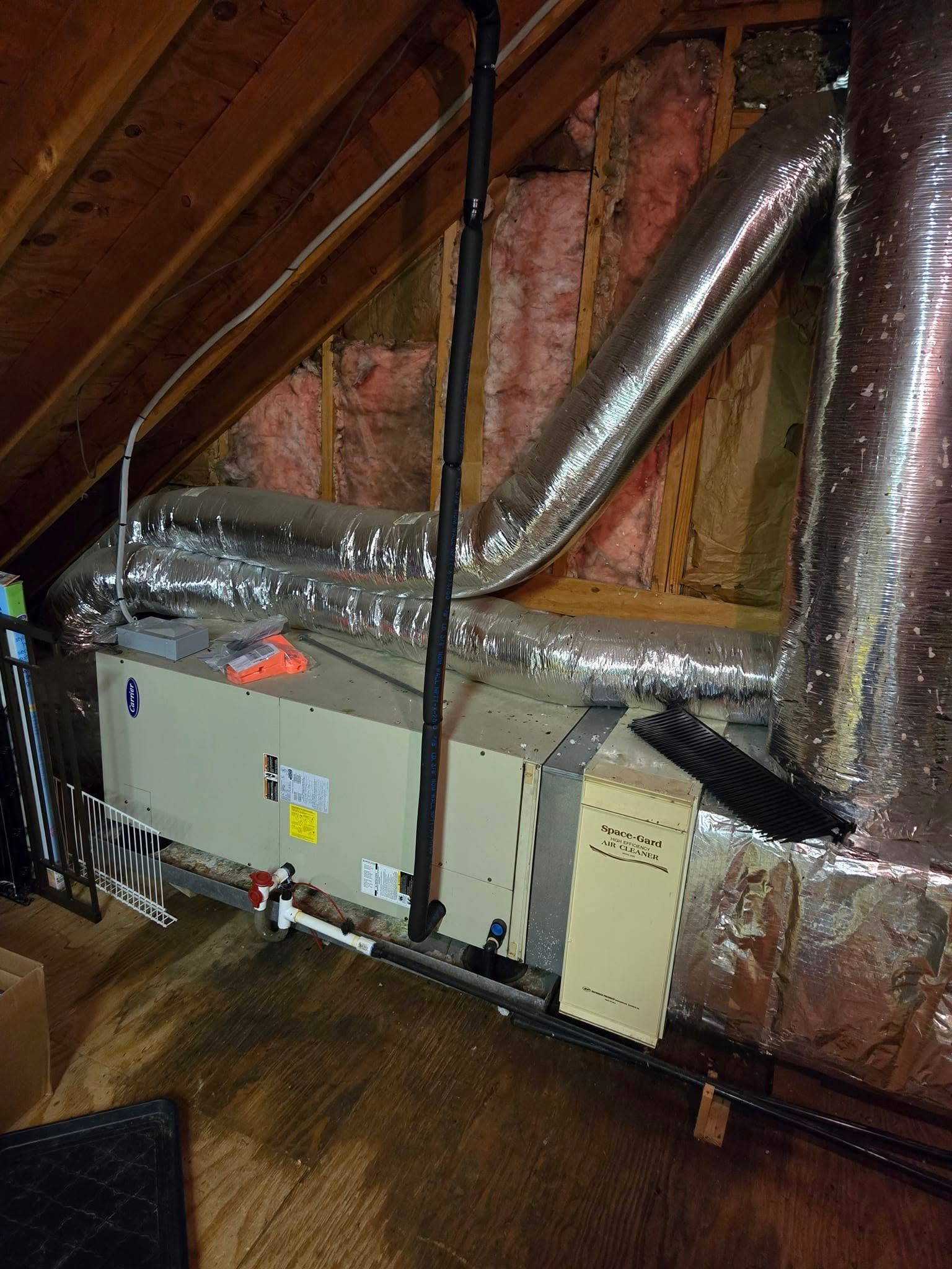 HVAC unit in an attic with ductwork, insulation, and black piping.