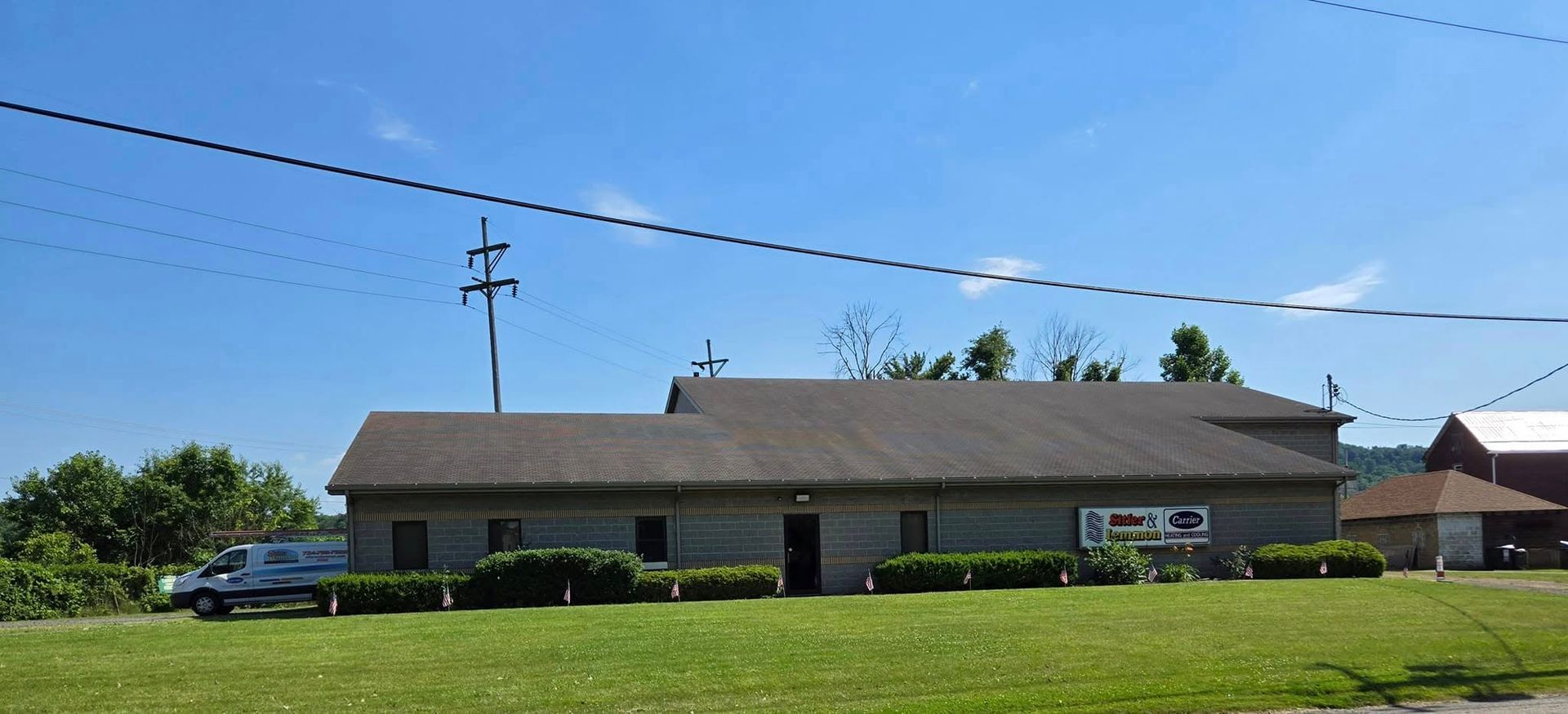 A gray building with a dark roof and a grassy lawn under a clear, blue sky.
