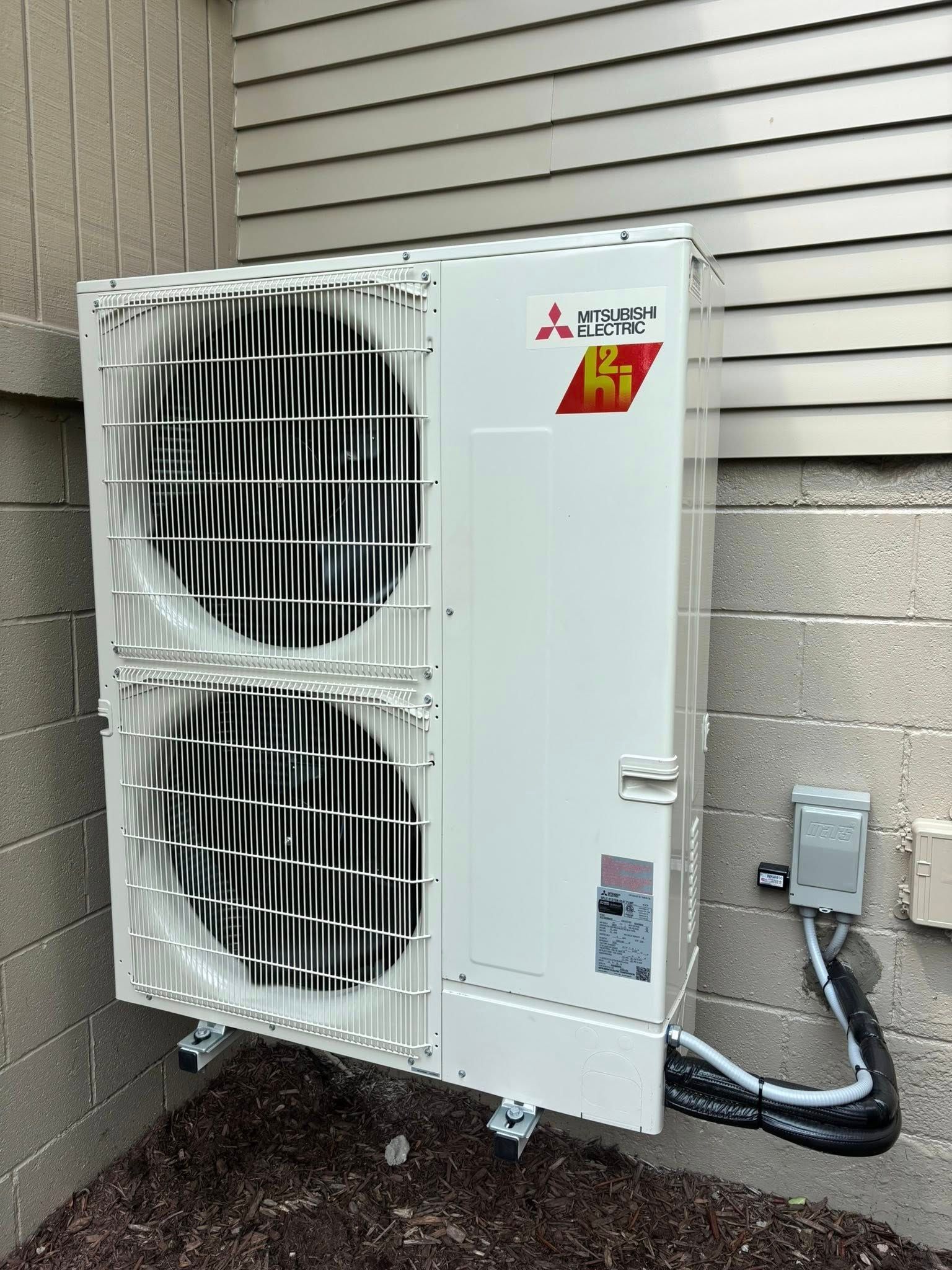 White Mitsubishi HVAC unit mounted on a beige building exterior with fans visible.
