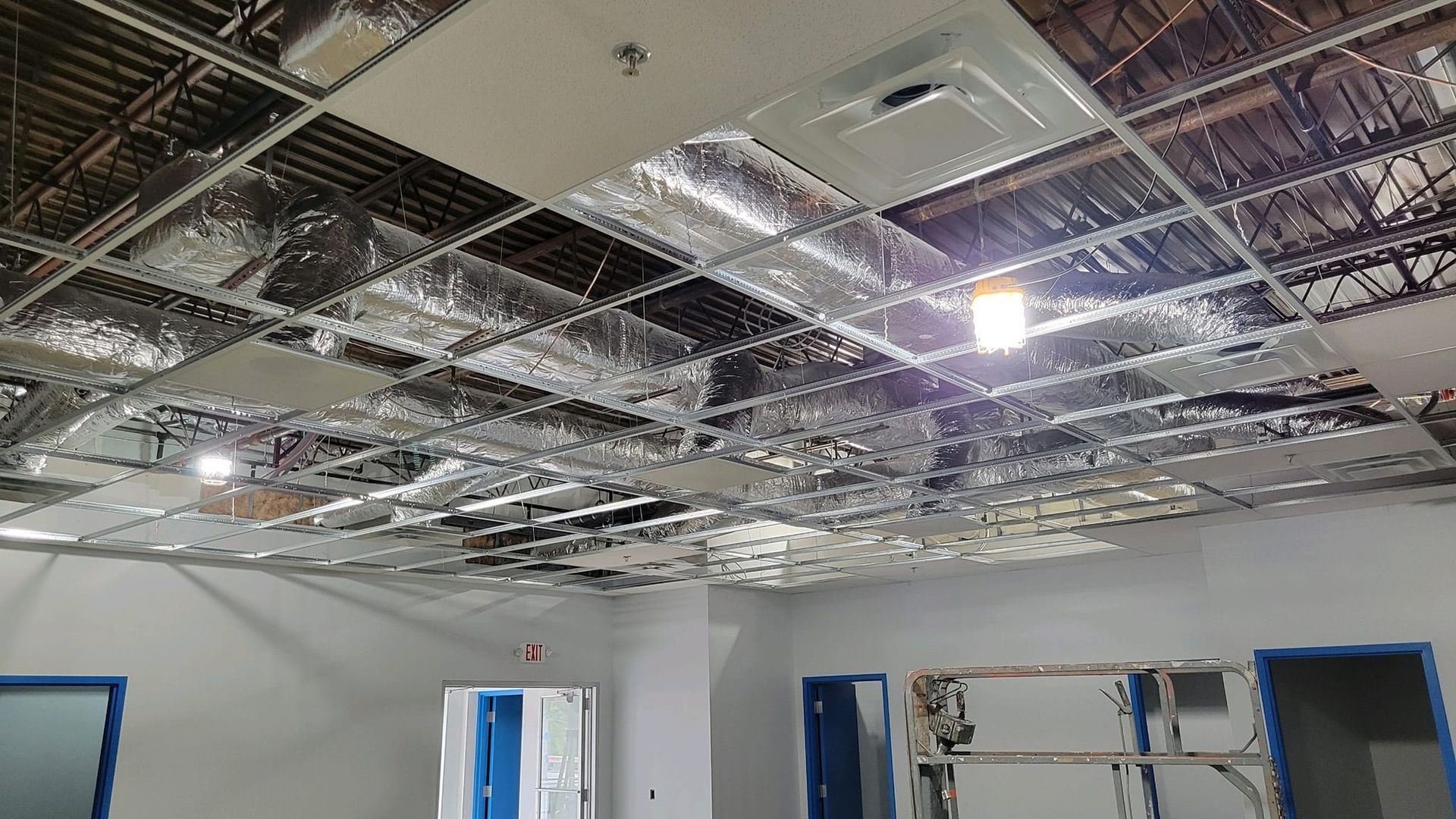 Ceiling construction in a room, with exposed metal grid, insulation, and some ceiling tiles installed.