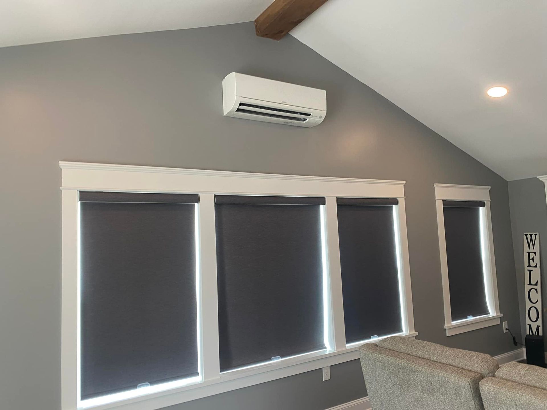 Gray wall with windows, dark roller shades, and an AC unit.