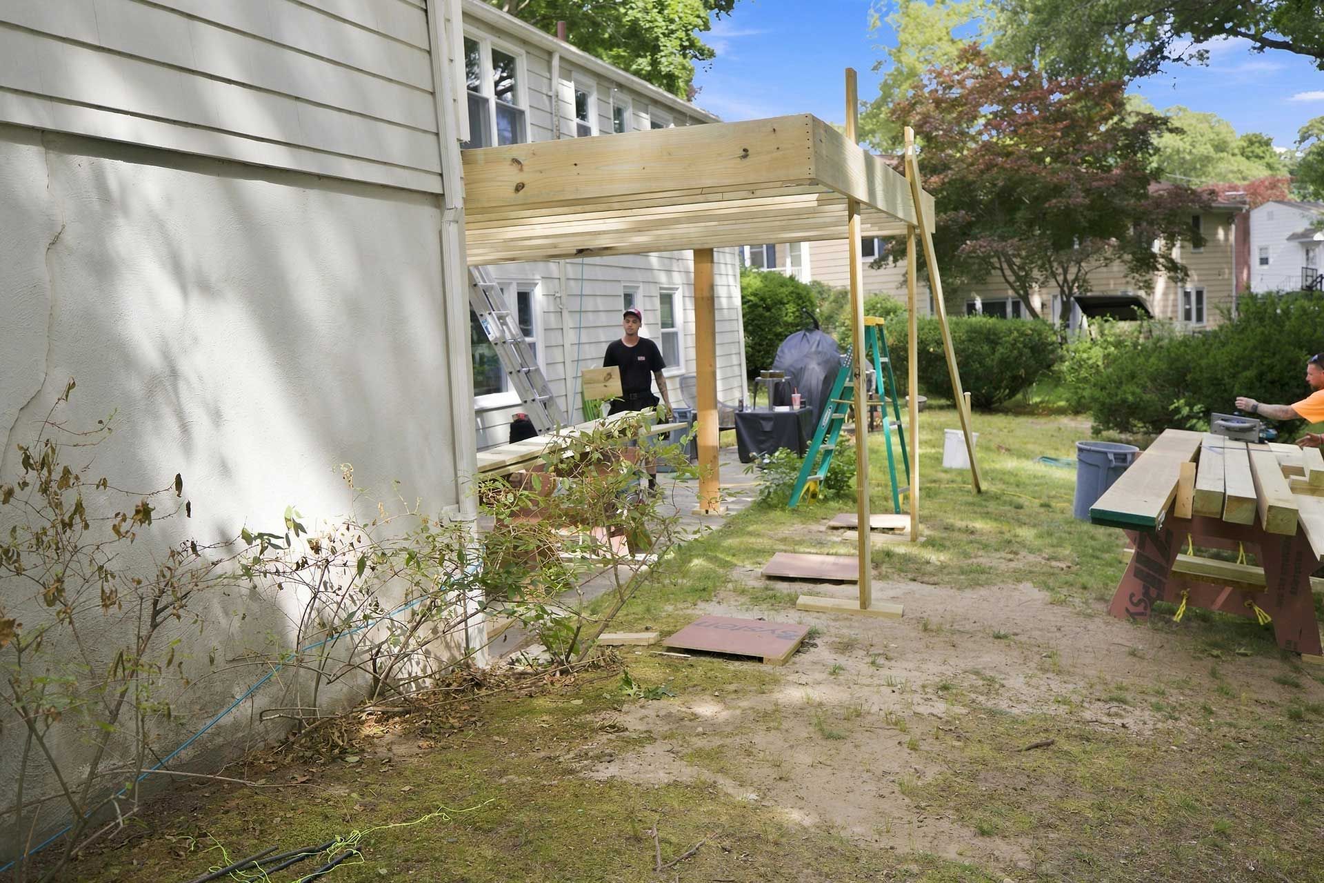 Backyard with a partially built wooden deck beside a house, with tools and lumber on the ground