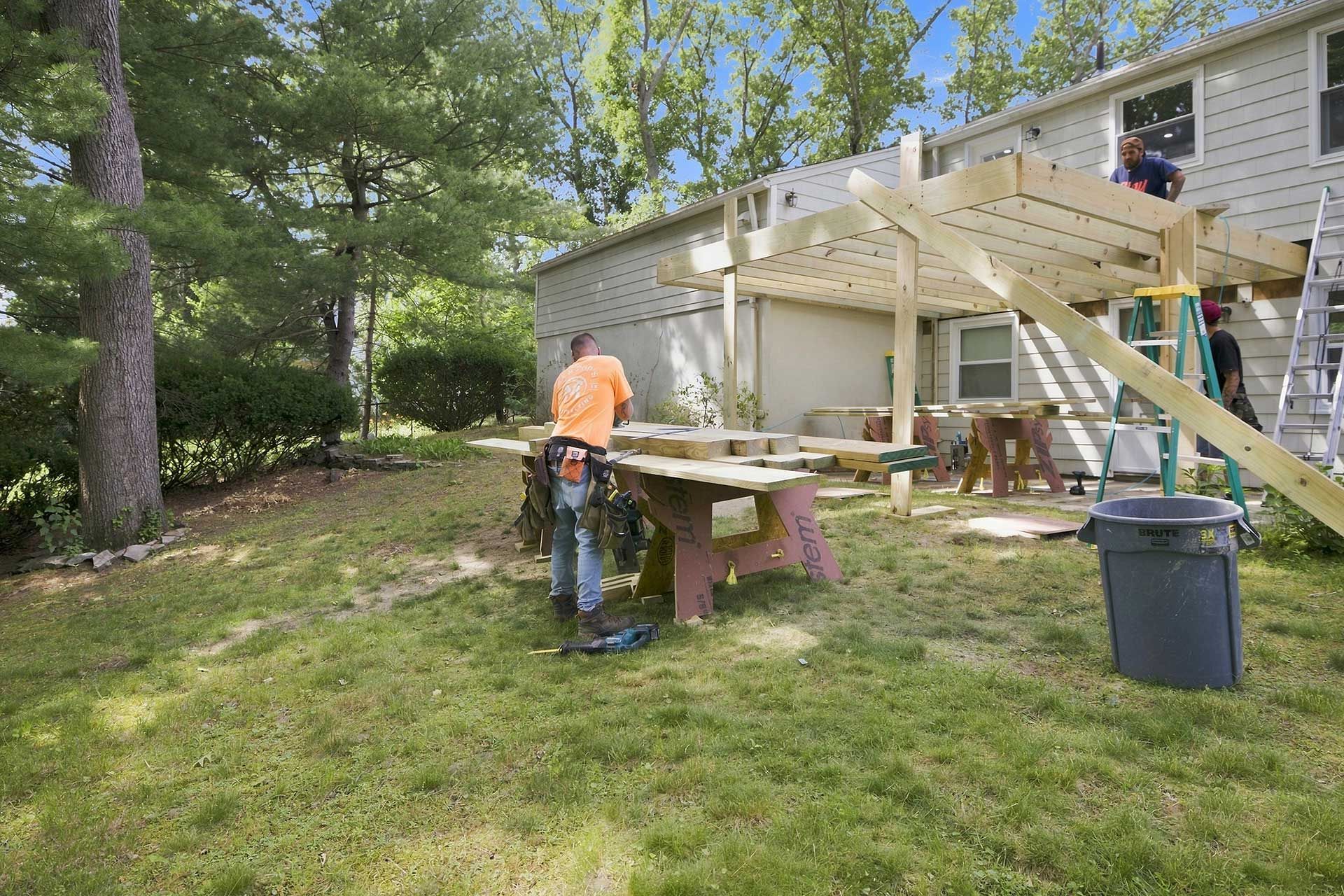 Person using a saw to cut wood on a backyard deck beside a house and trees