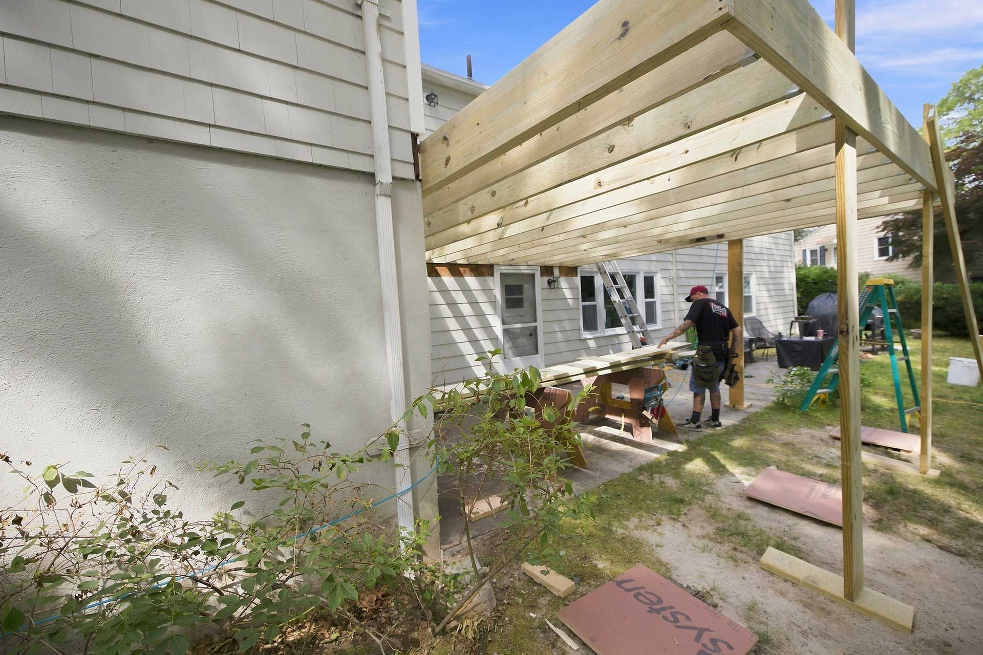 Backyard deck under construction beside a house, with a worker and tools visible.