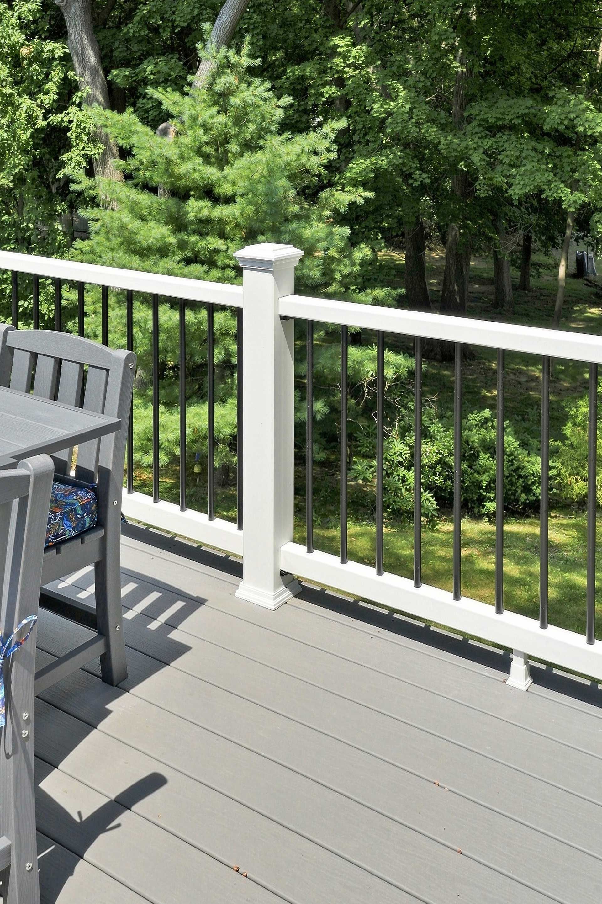 Wooden deck with white railing and black chairs overlooking green trees and a garden